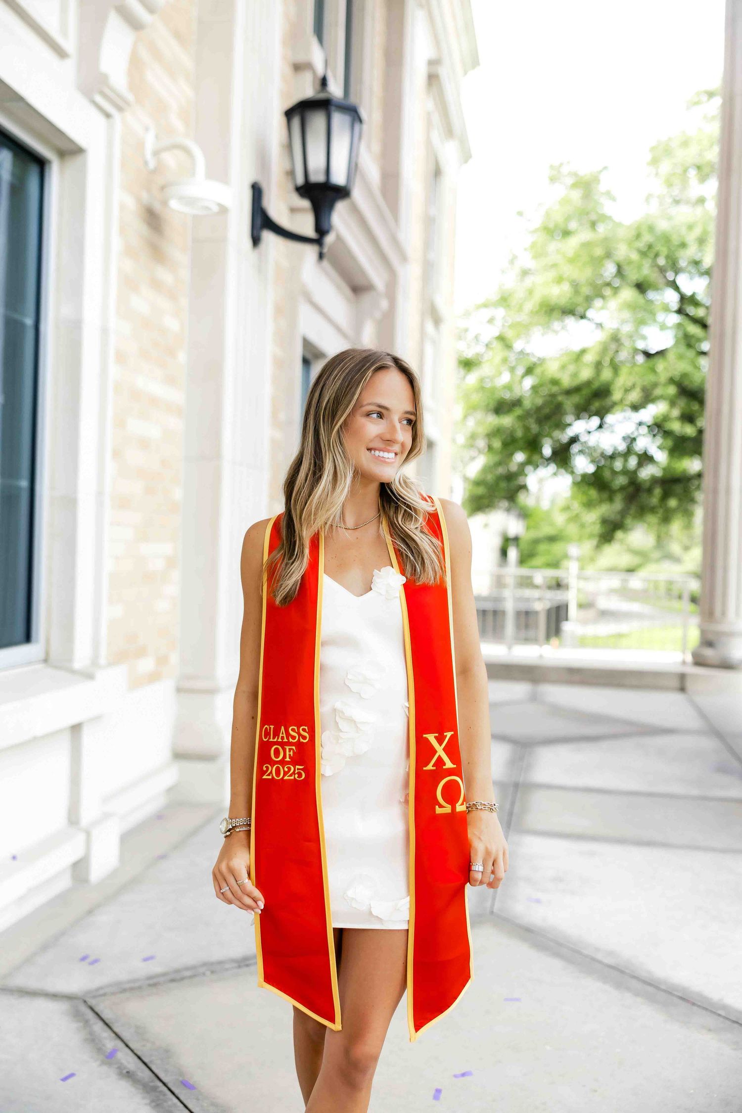 Graduate wearing a red academic stole poses outside a stone building.