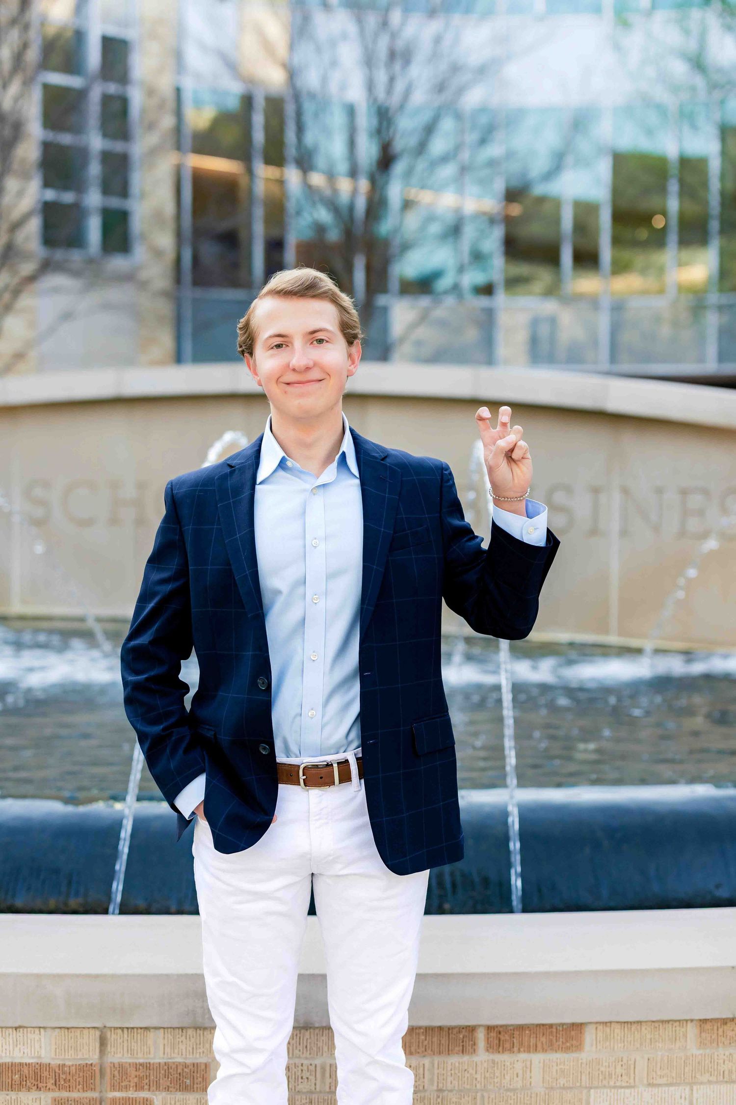Professional wearing navy blazer and white pants poses by outdoor fountain at college campus.
TCU Graduation photographer