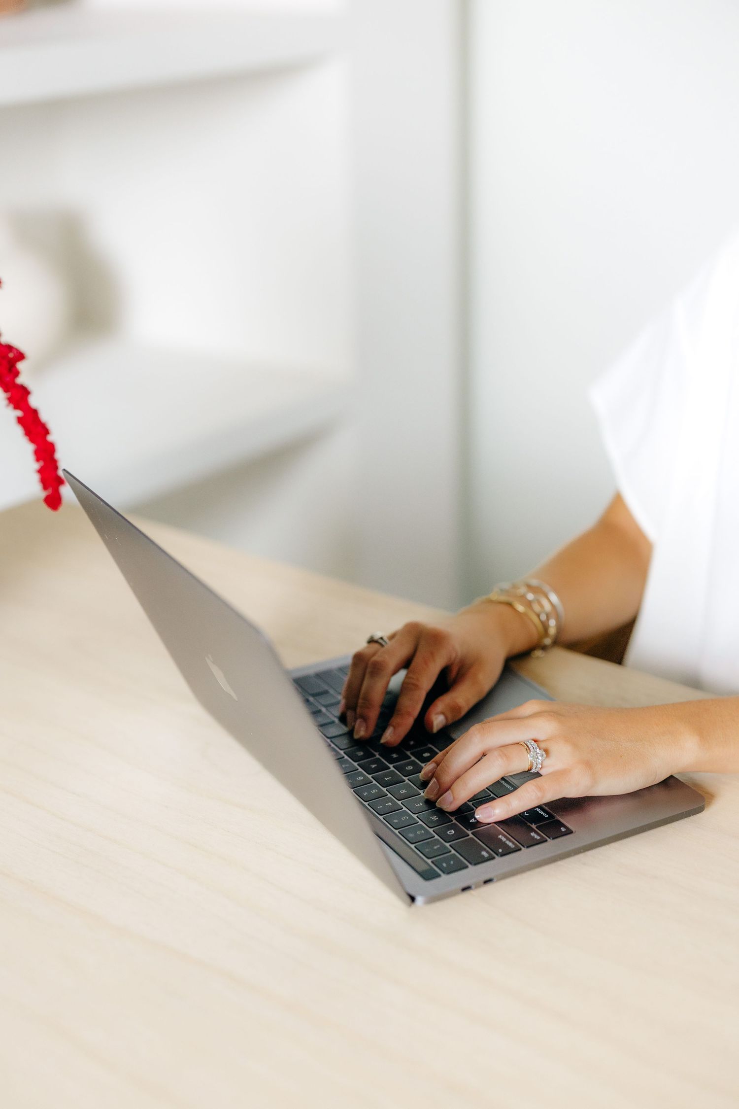 Hands with wedding rings type on MacBook laptop against white background.