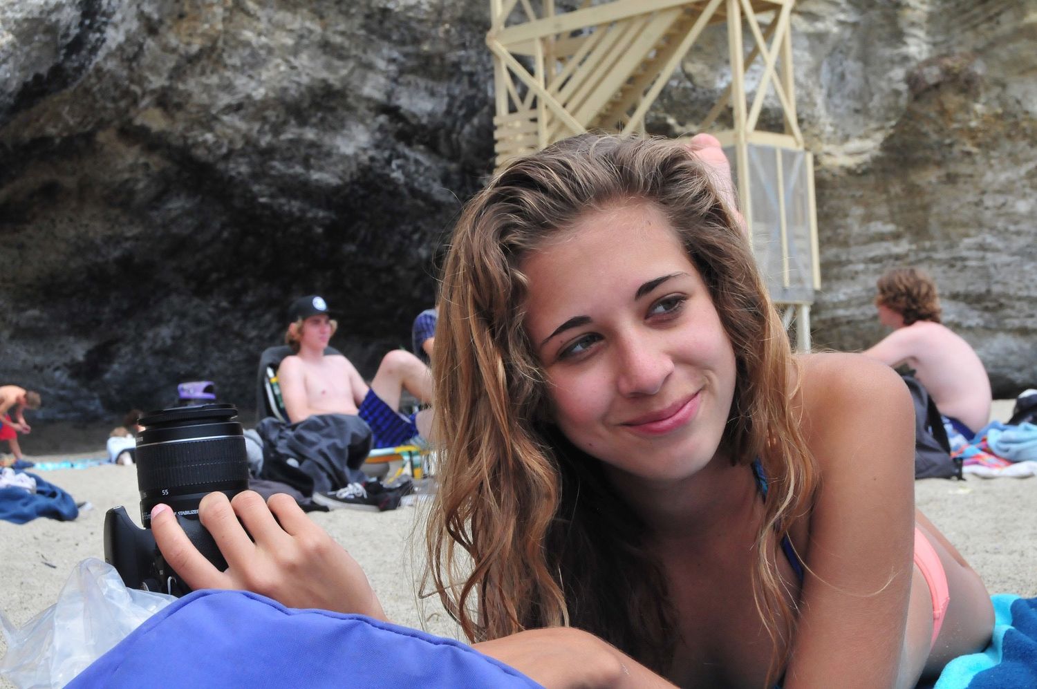 Beach photographer relaxing on blanket with camera equipment.