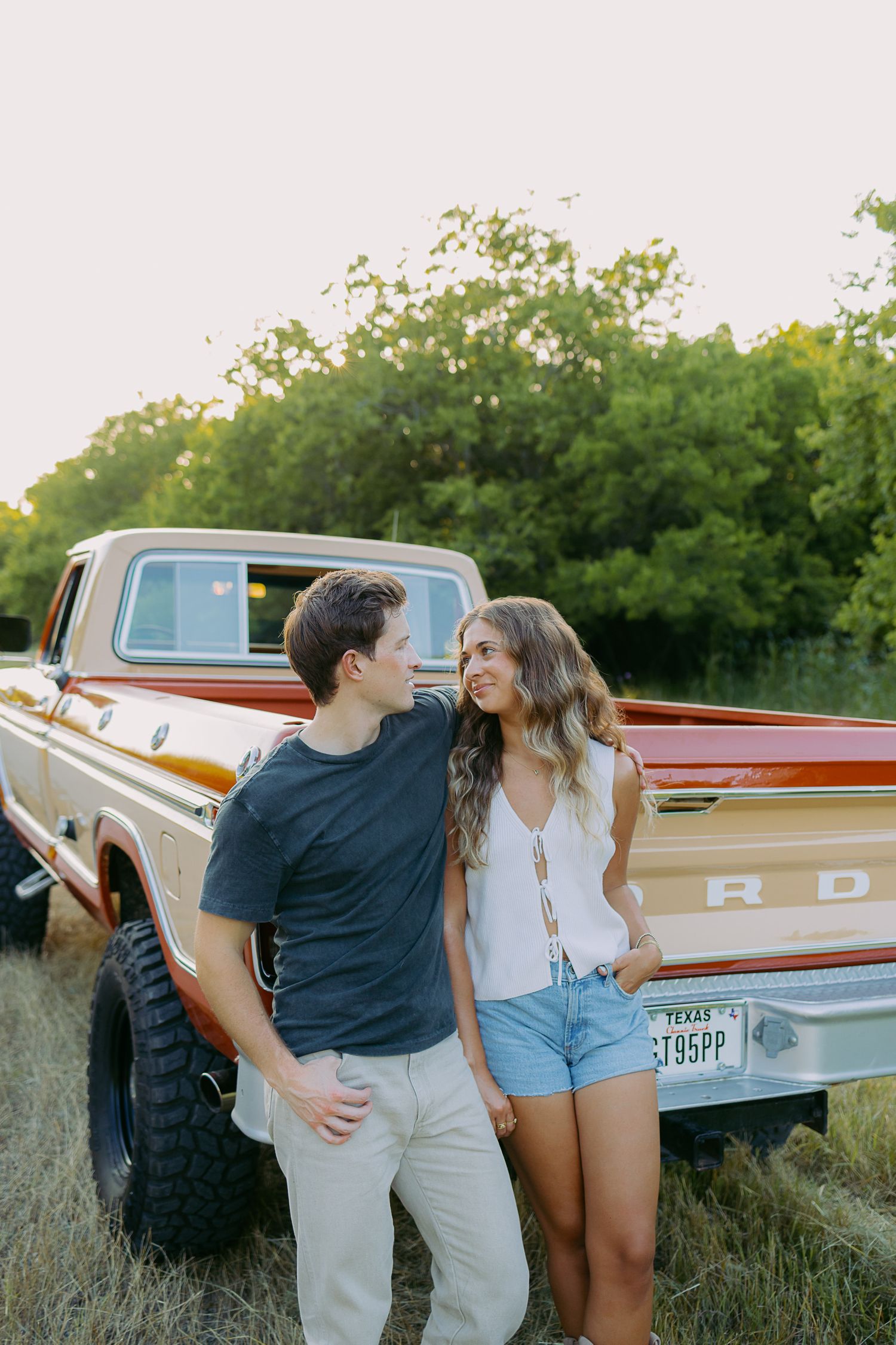 Couple embracing next to vintage aircraft during sunset photoshoot in grassy field.