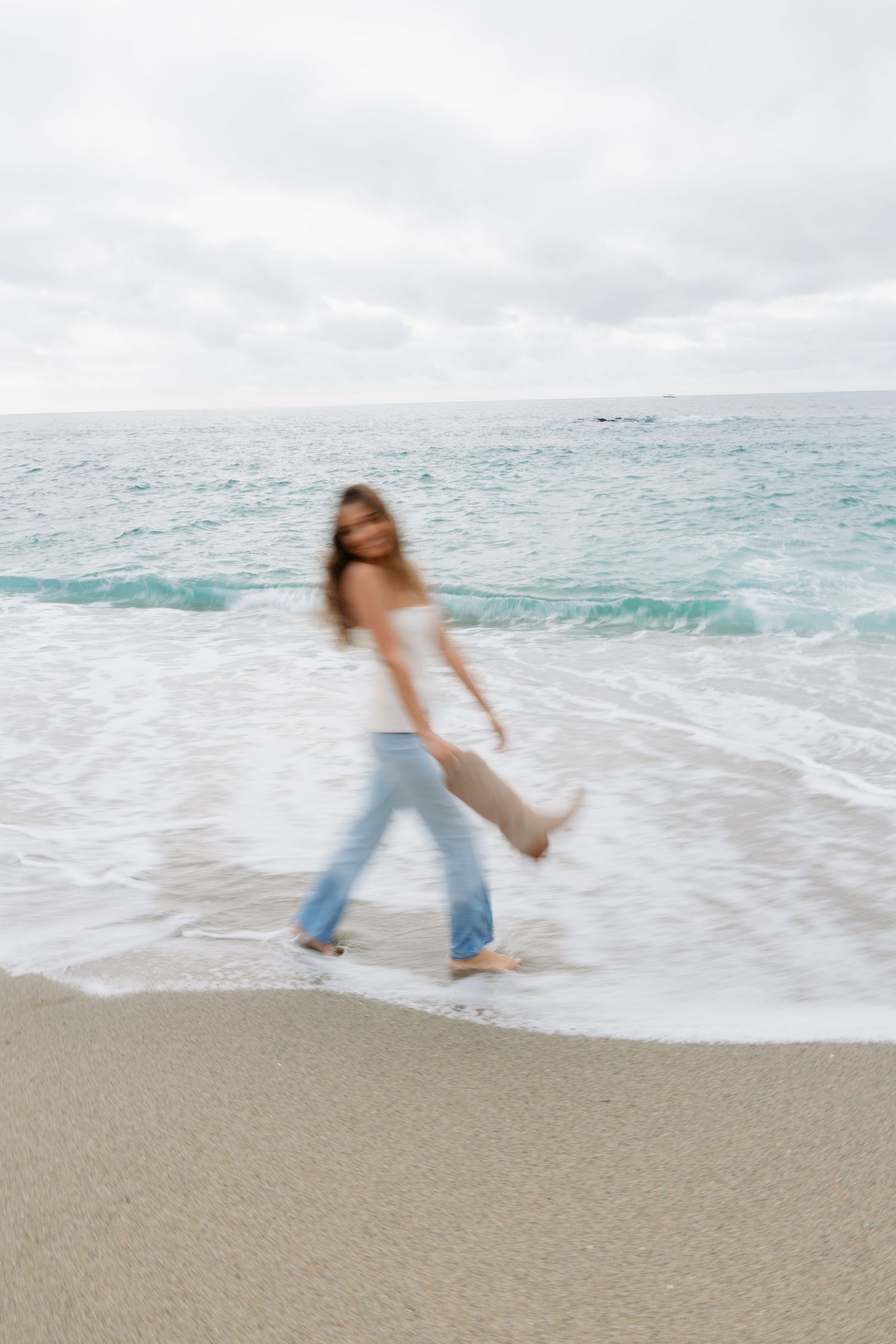 Motion blur captures a person dancing and twirling on a sandy beach with turquoise ocean waves in the background.