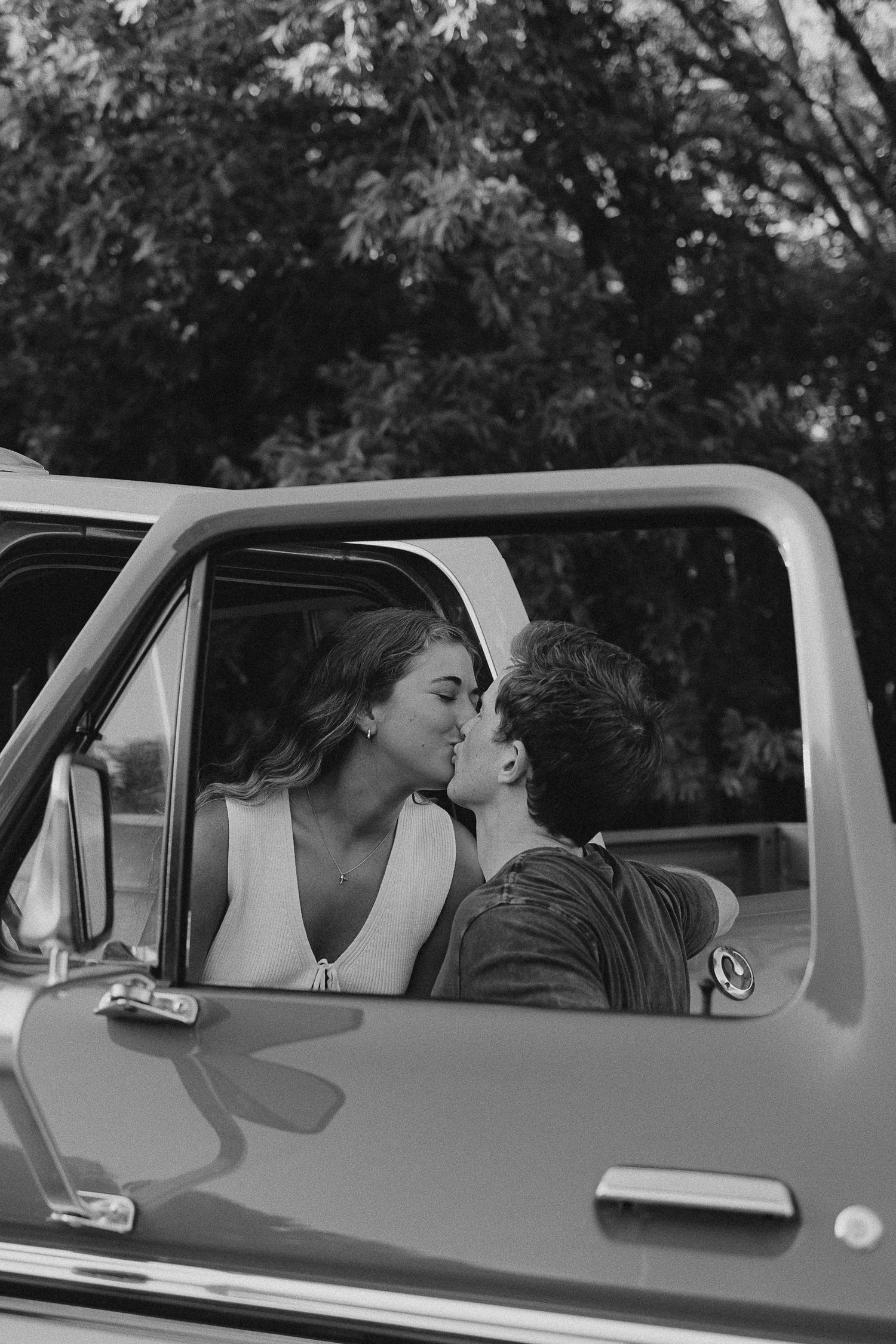 A romantic black and white photo of a couple sharing an intimate moment in a vintage pickup truck.