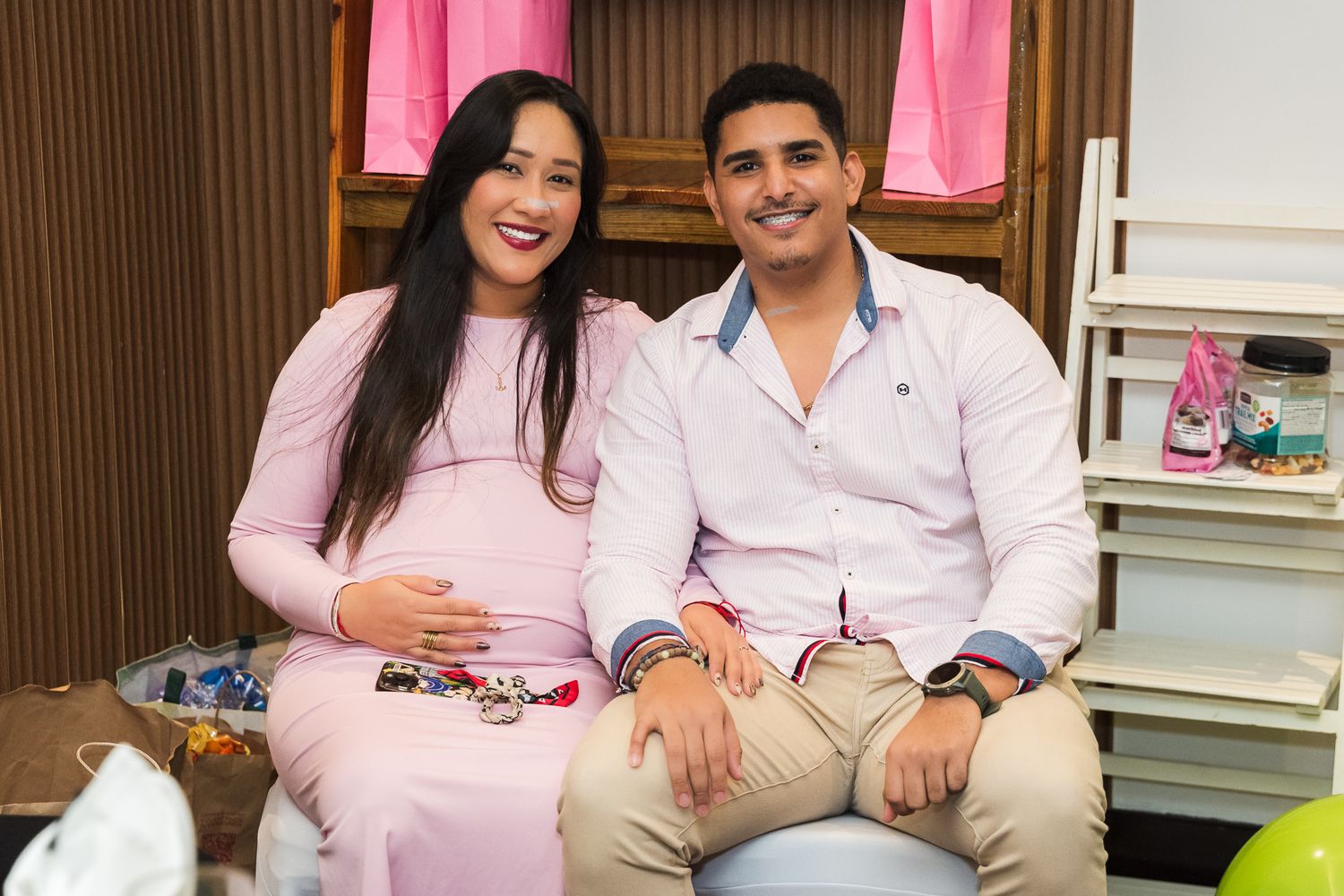 A couple sits together on white furniture in a pink themed room with wood paneled walls.