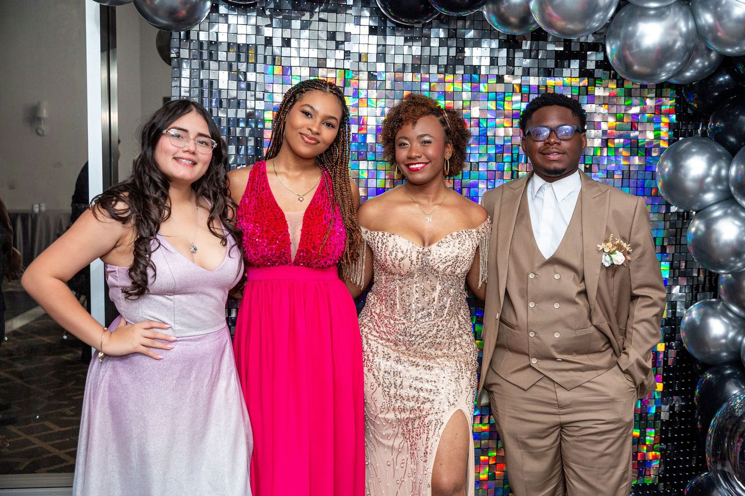 Four people pose together at a formal event with silver balloons and colorful stained glass windows in the background.