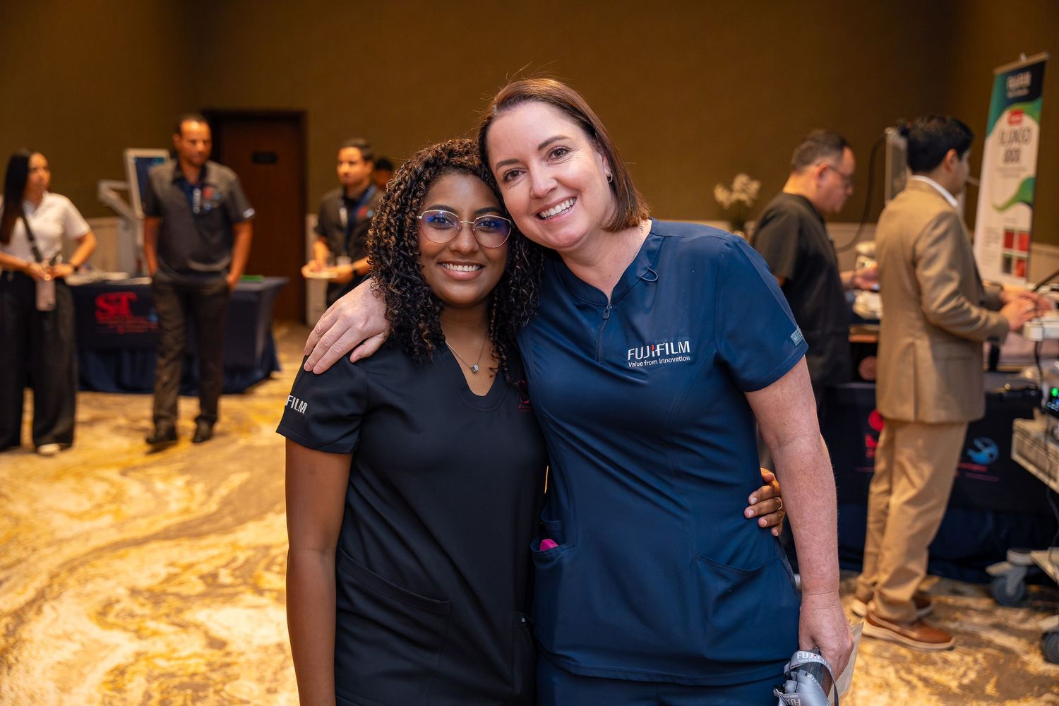 Two healthcare professionals in scrubs smile together at a medical conference event.