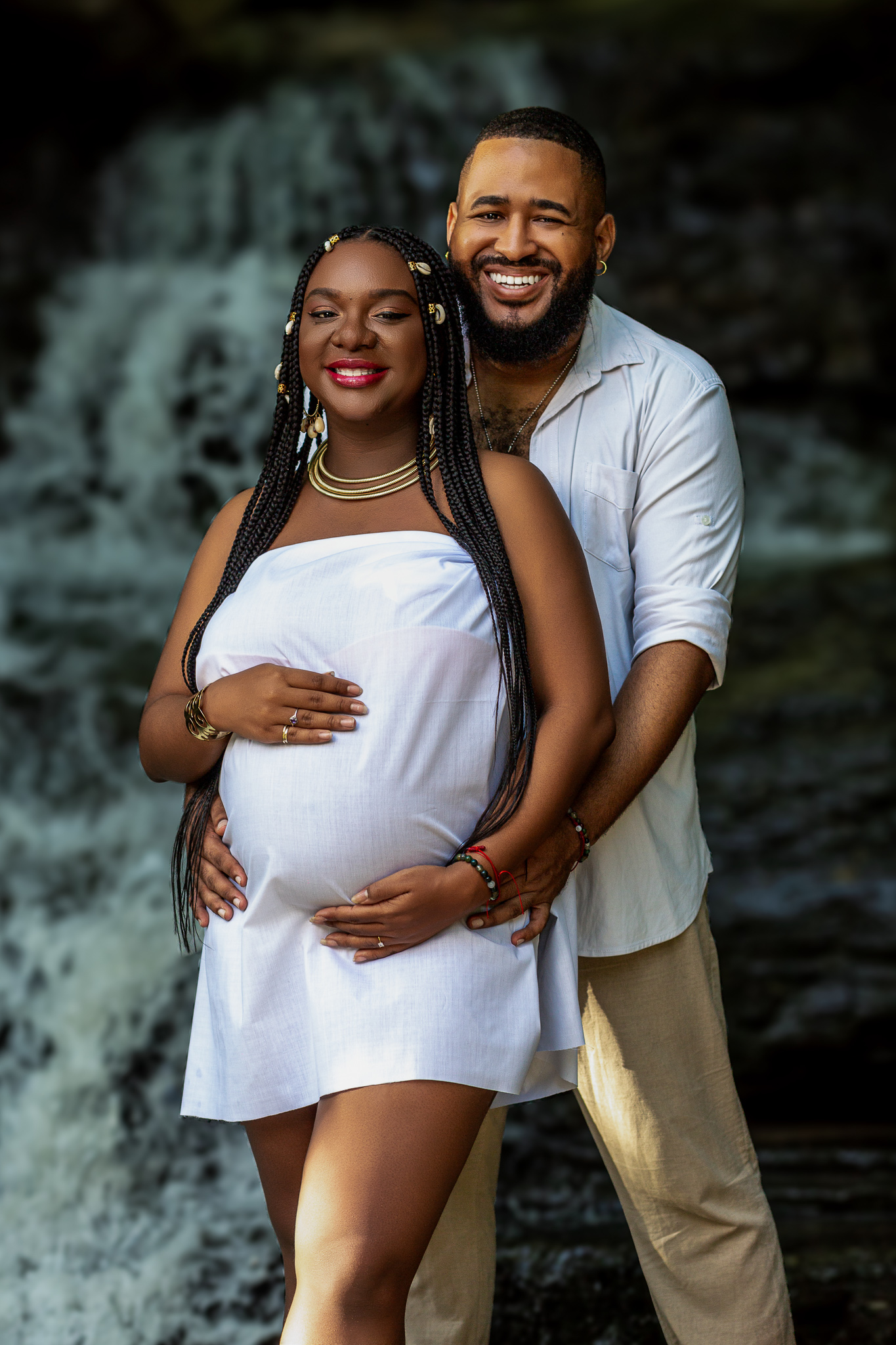 Romantic maternity photo of couple embracing by waterfall.