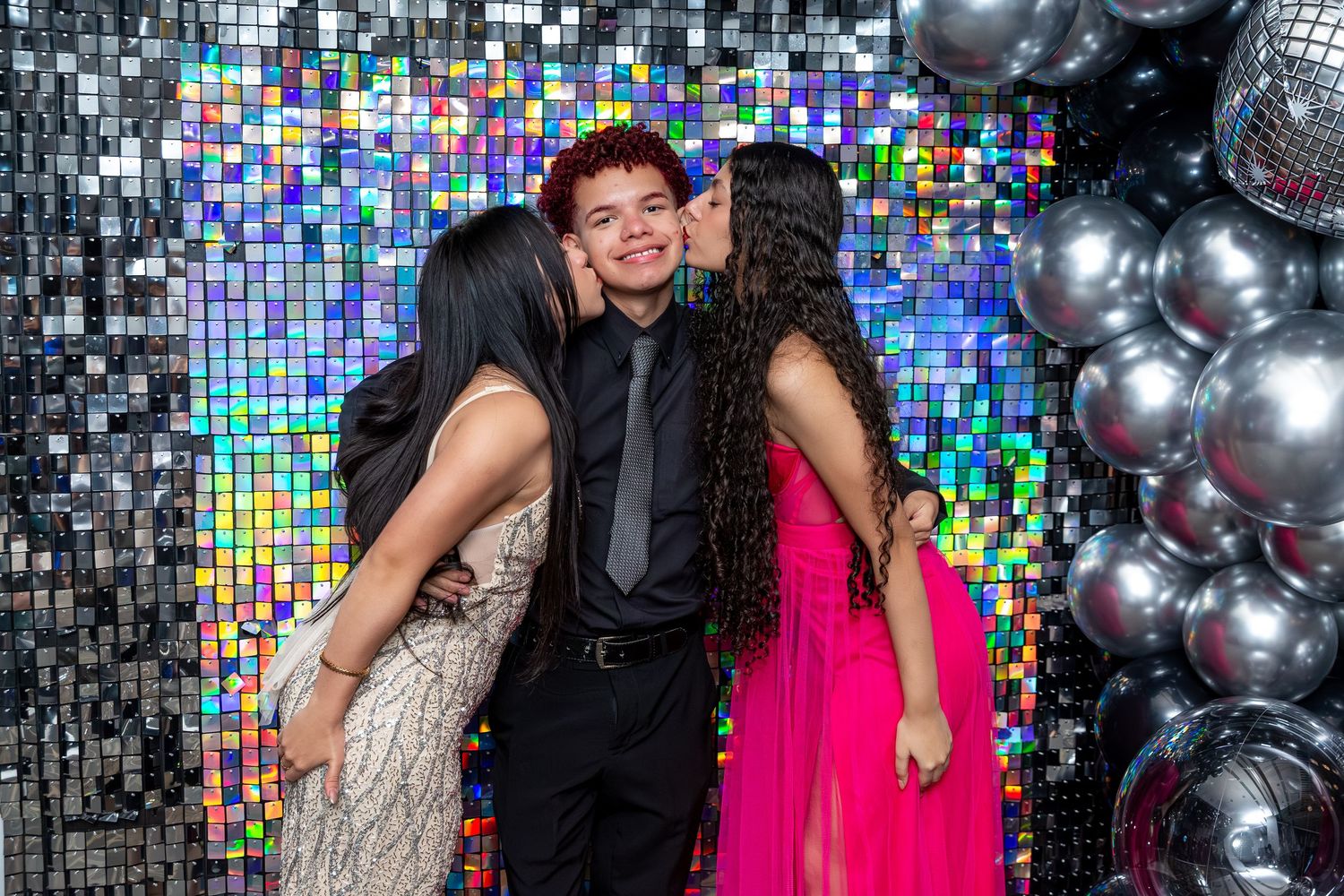 People posing together at a party with silver disco balls and colorful mosaic backdrop creating a festive atmosphere.
