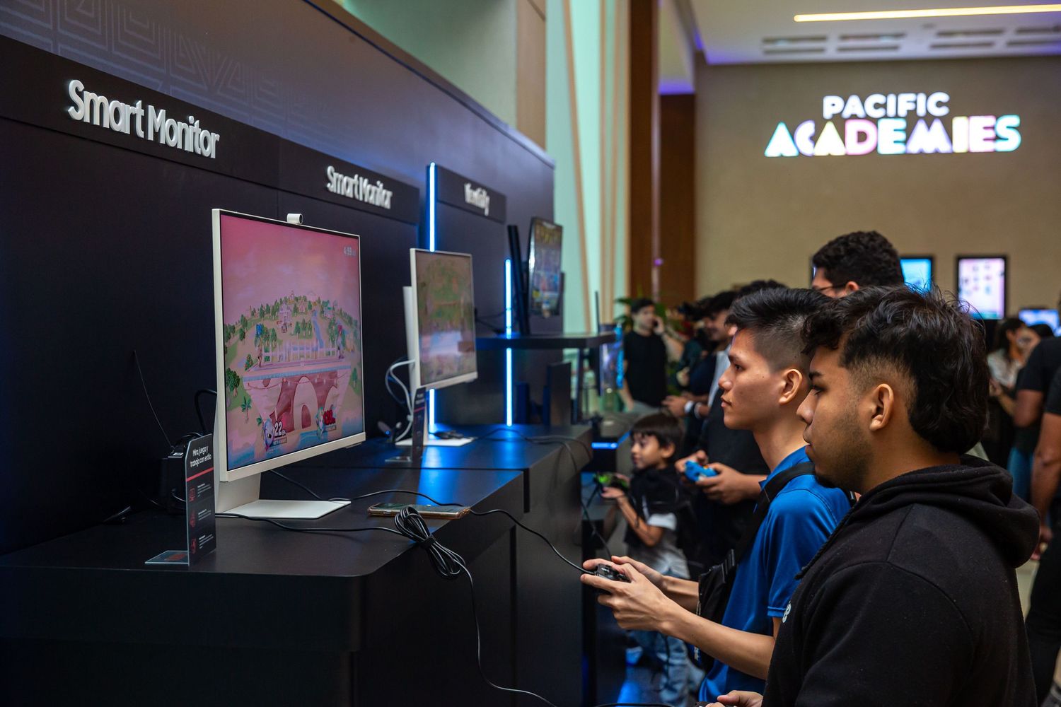 A group of people, mostly young boys, are gathered around a large screen displaying a video game or interactive display.