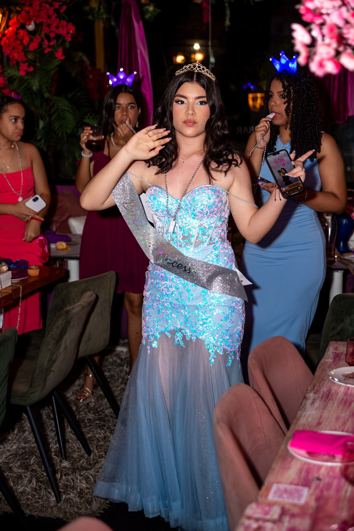 A celebratory party scene with blue tulle dresses and pink decorative lighting creates a festive atmosphere.