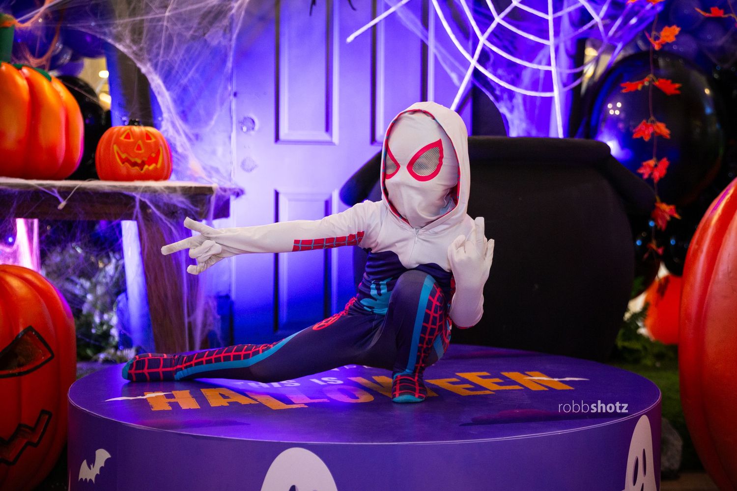 Halloween scene with Spider-Gwen costume and spooky decorations in purple lighting.