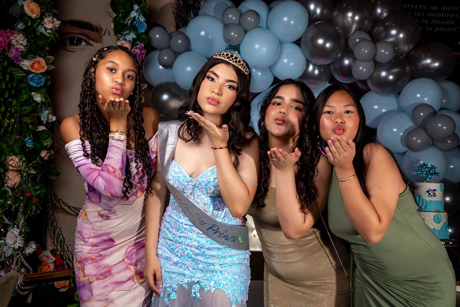 Friends pose together at a party with blue balloon decorations and festive lighting in the background.