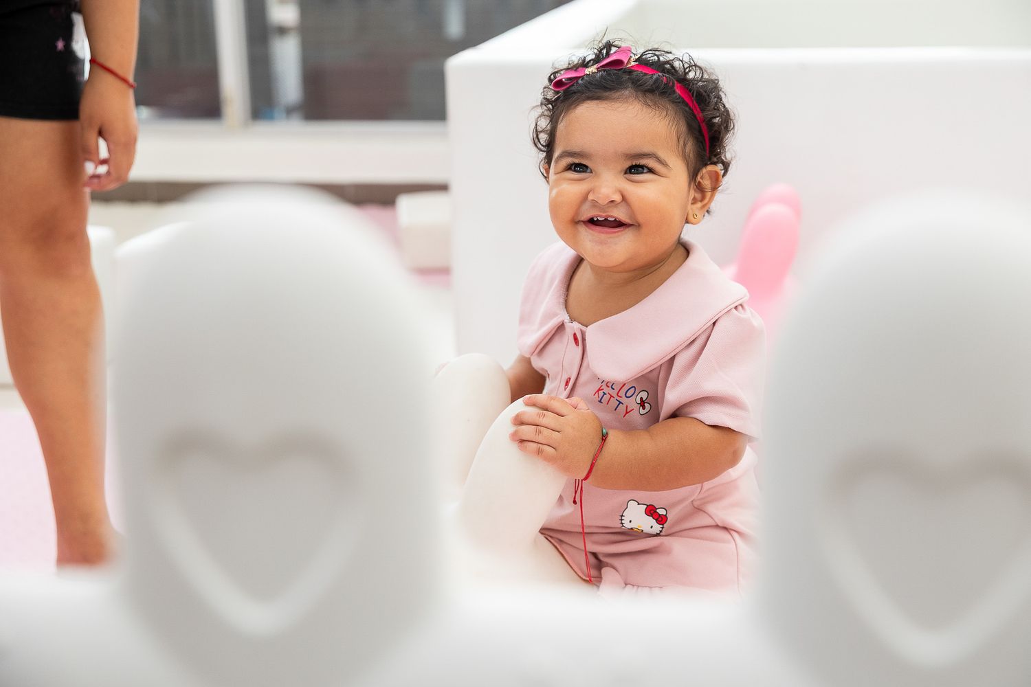 Smiling baby girl in pink Hello Kitty outfit with floral headband at a birthday party.