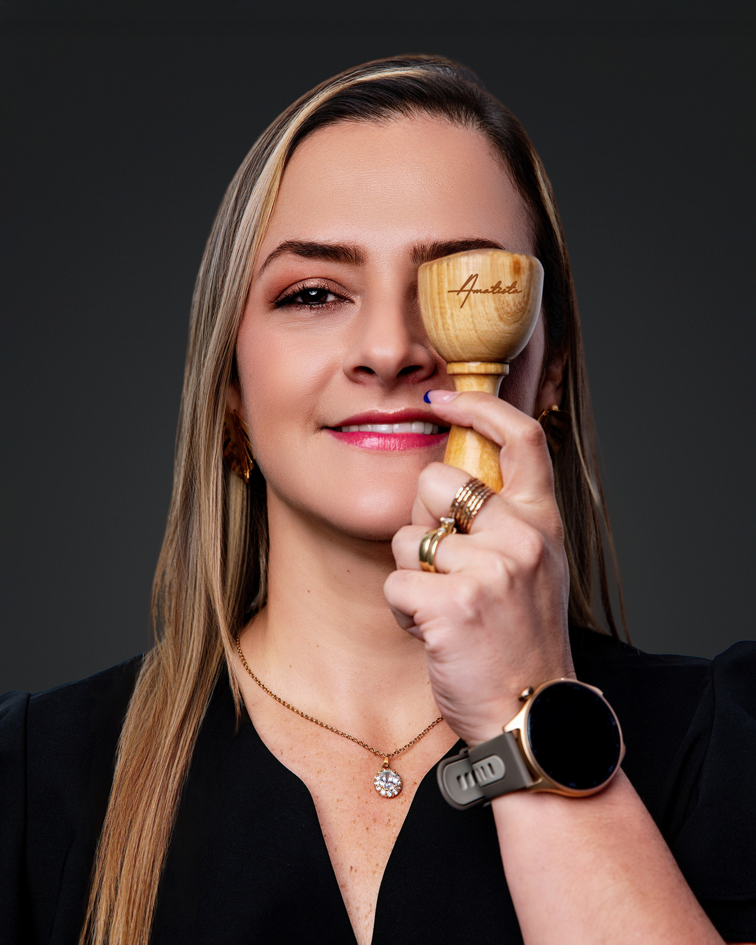 A person wearing a black top and jewelry holds a golden trophy cup against a dark background.
