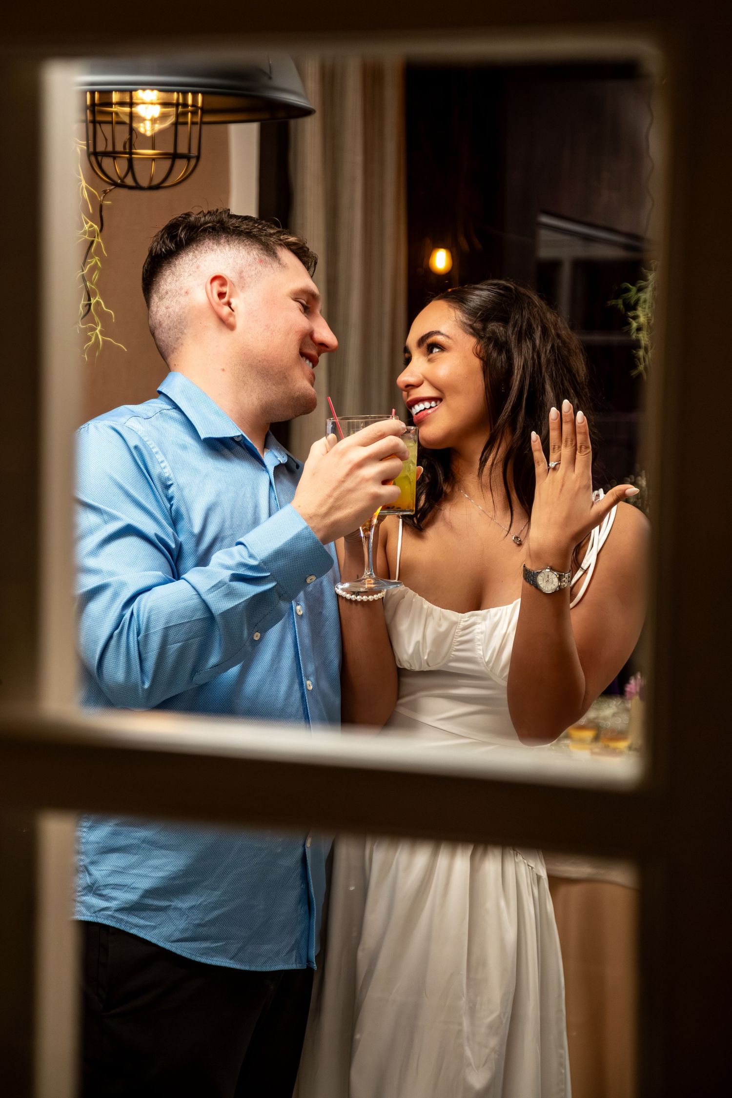 A romantic couple shares drinks and laughter at a dimly lit bar with warm lighting and industrial decor.