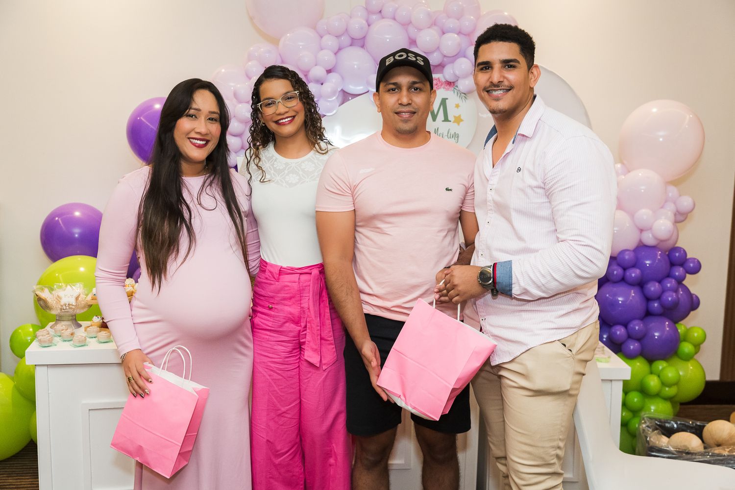 Group photo at a baby shower celebration with pink and purple balloon decorations in the background.