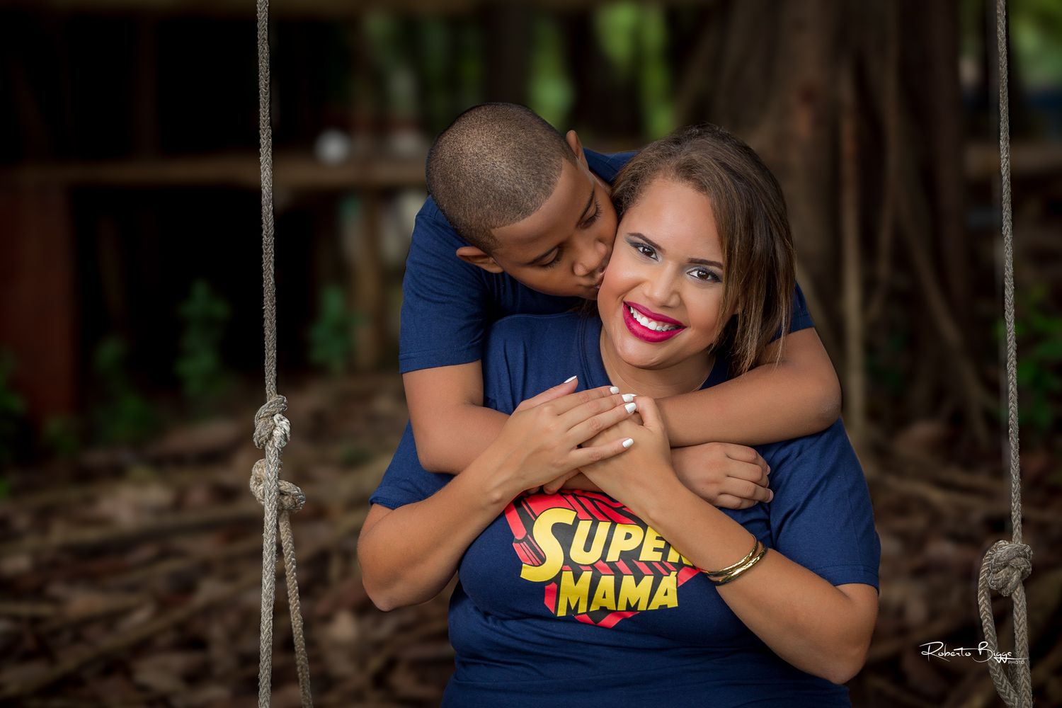 A loving couple in matching navy blue t-shirts embrace outdoors in a natural wooded setting.