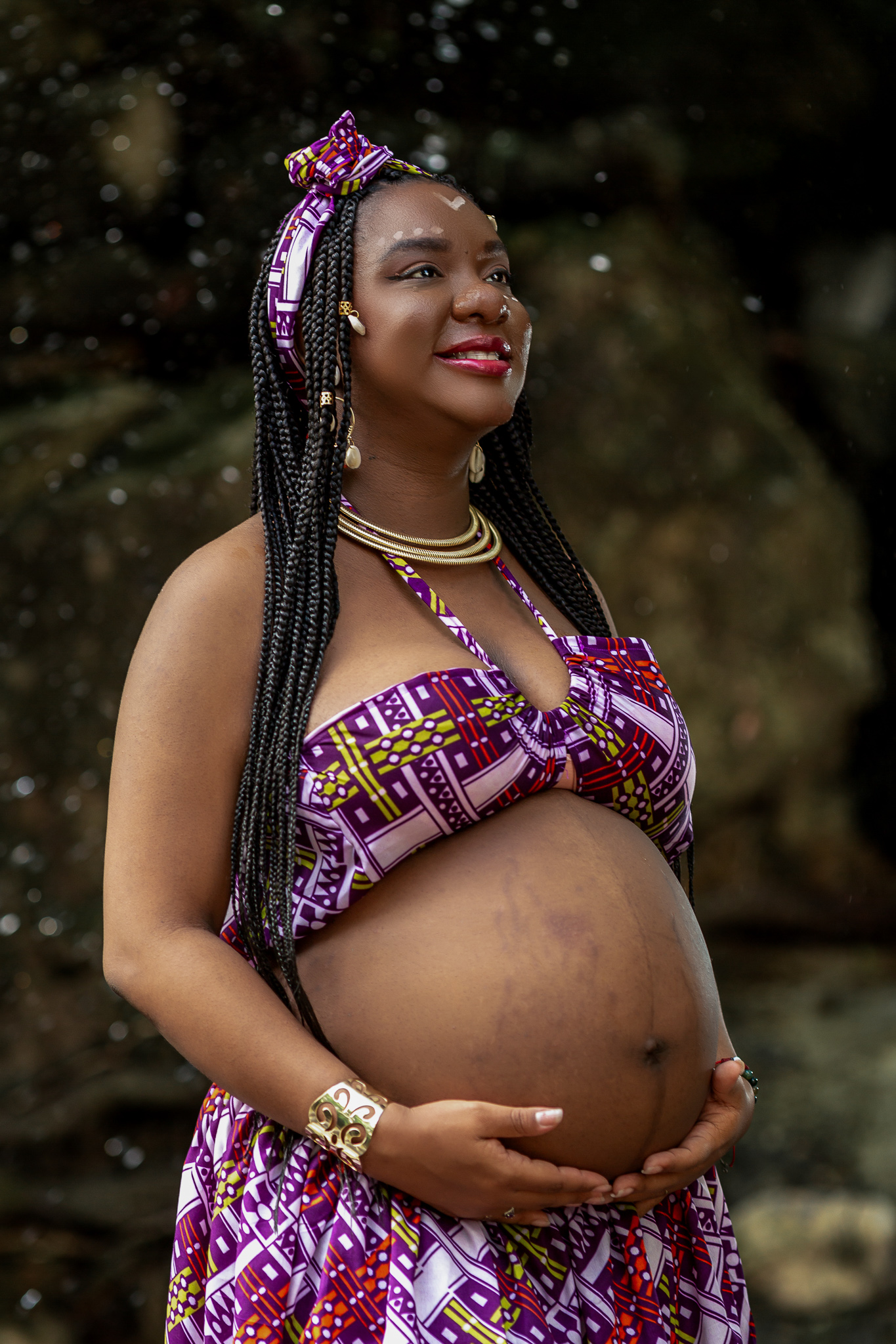 Glowing expectant mother in vibrant African print dress poses outdoors.