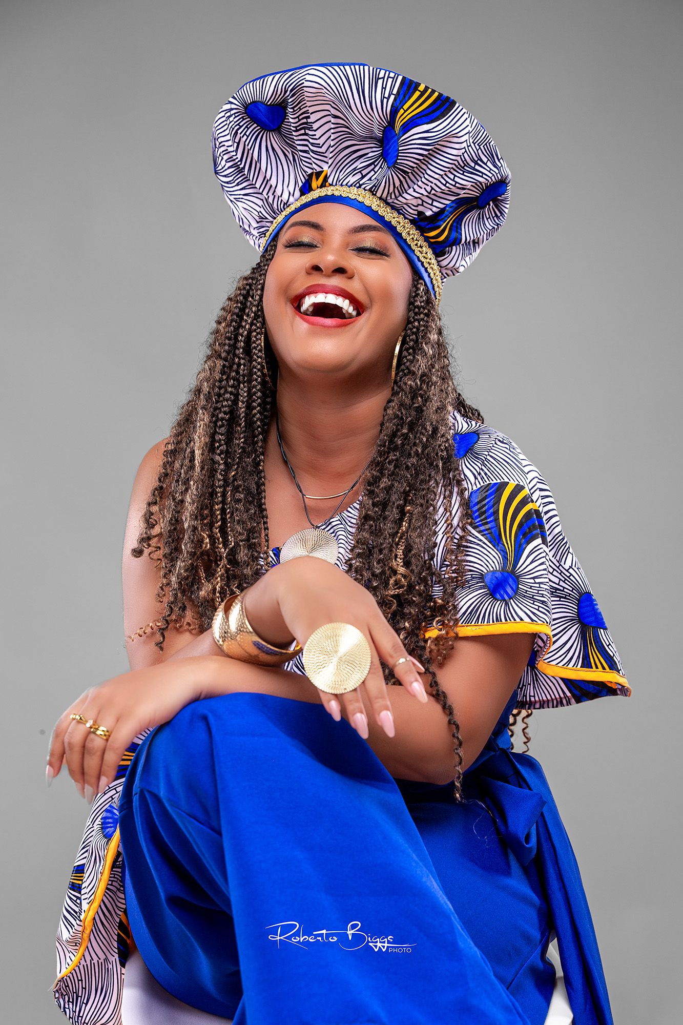 Stylish portraits in a blue dress and patterned headwrap against grey background showing genuine laughter.