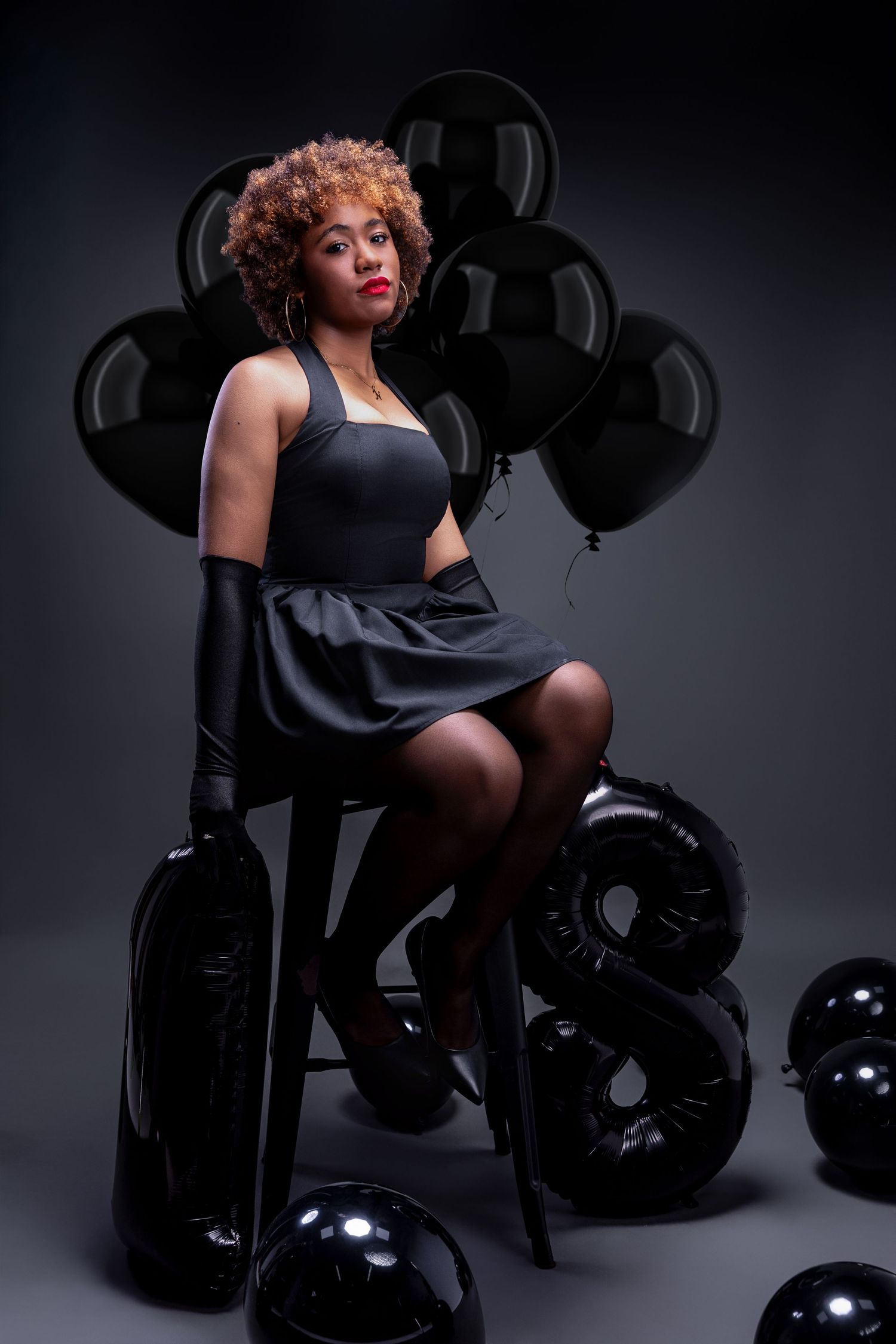 A dramatic fashion photoshoot featuring a model in black attire posing with motorcycle helmets against a dark background.