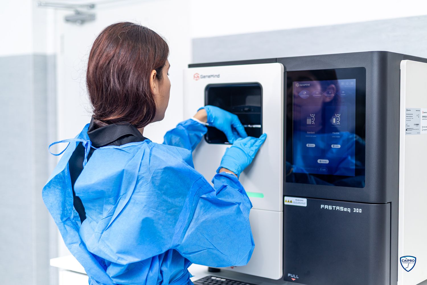 A person in a blue protective suit operating a medical screening device in a hospital or medical facility.