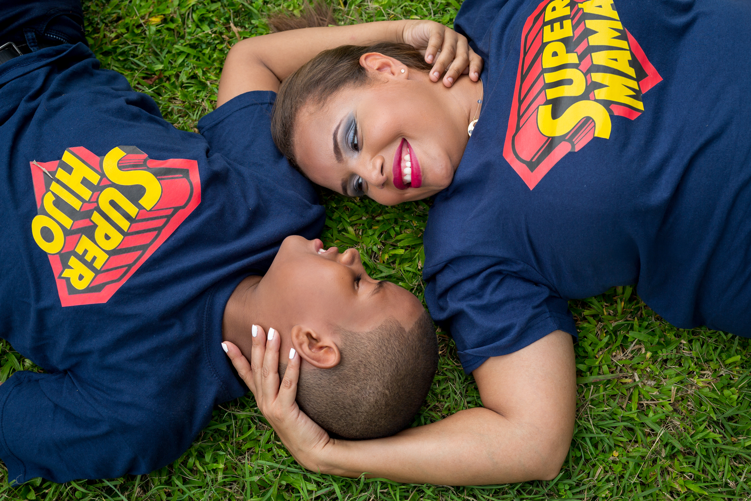 Couple in matching navy shirts lying on grass smiling at each other.