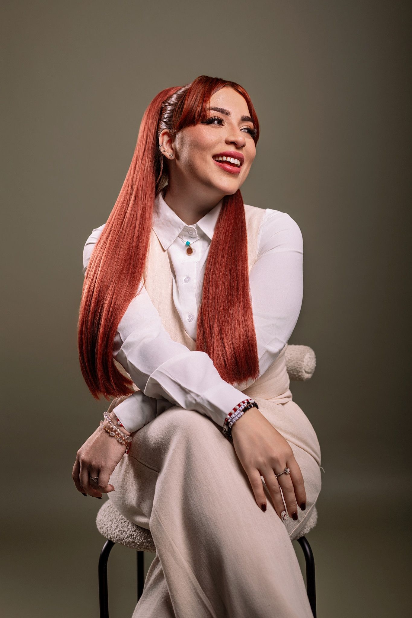 A figure in a white outfit and vibrant red hair poses expressively in a series of studio portraits against a dark backdrop.