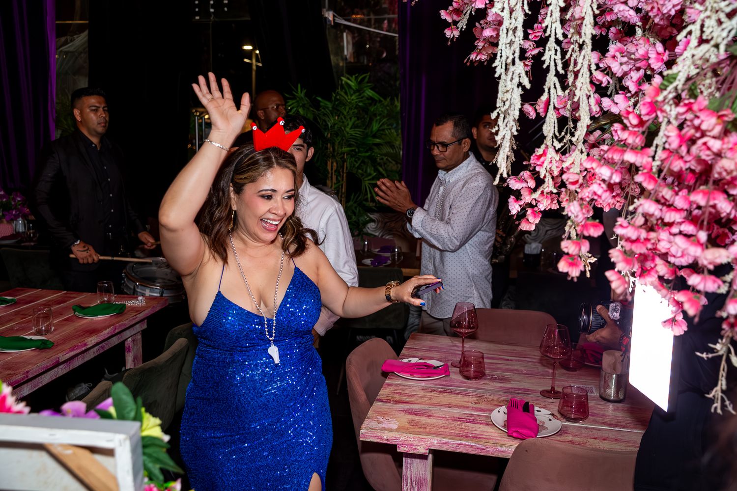 A person in a sparkly blue dress dances beneath pink cherry blossom decorations at a festive party venue.