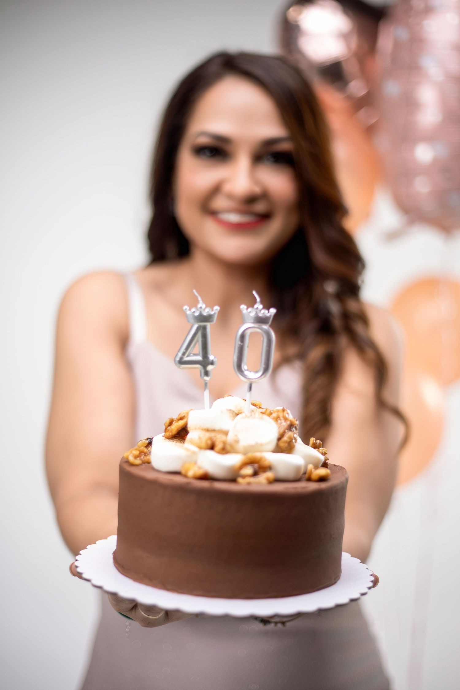 Woman smiling and holding a chocolate birthday cake with number 40 candles at her 40th birthday party.