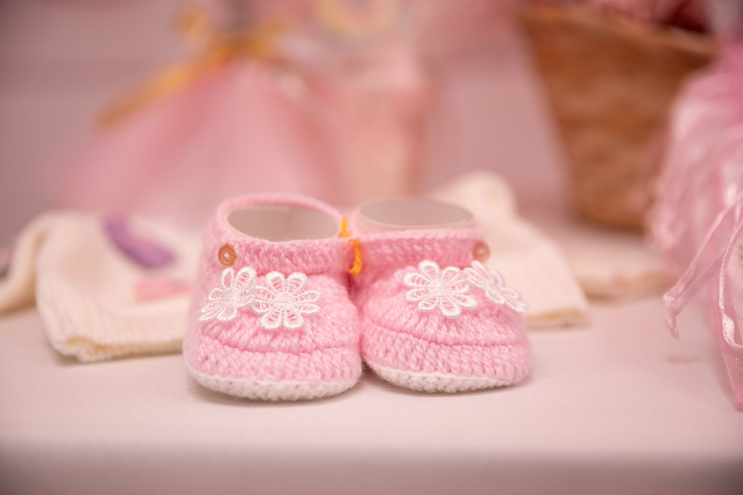 Pink knitted baby booties with white flower embellishments displayed on a table at a baby shower.