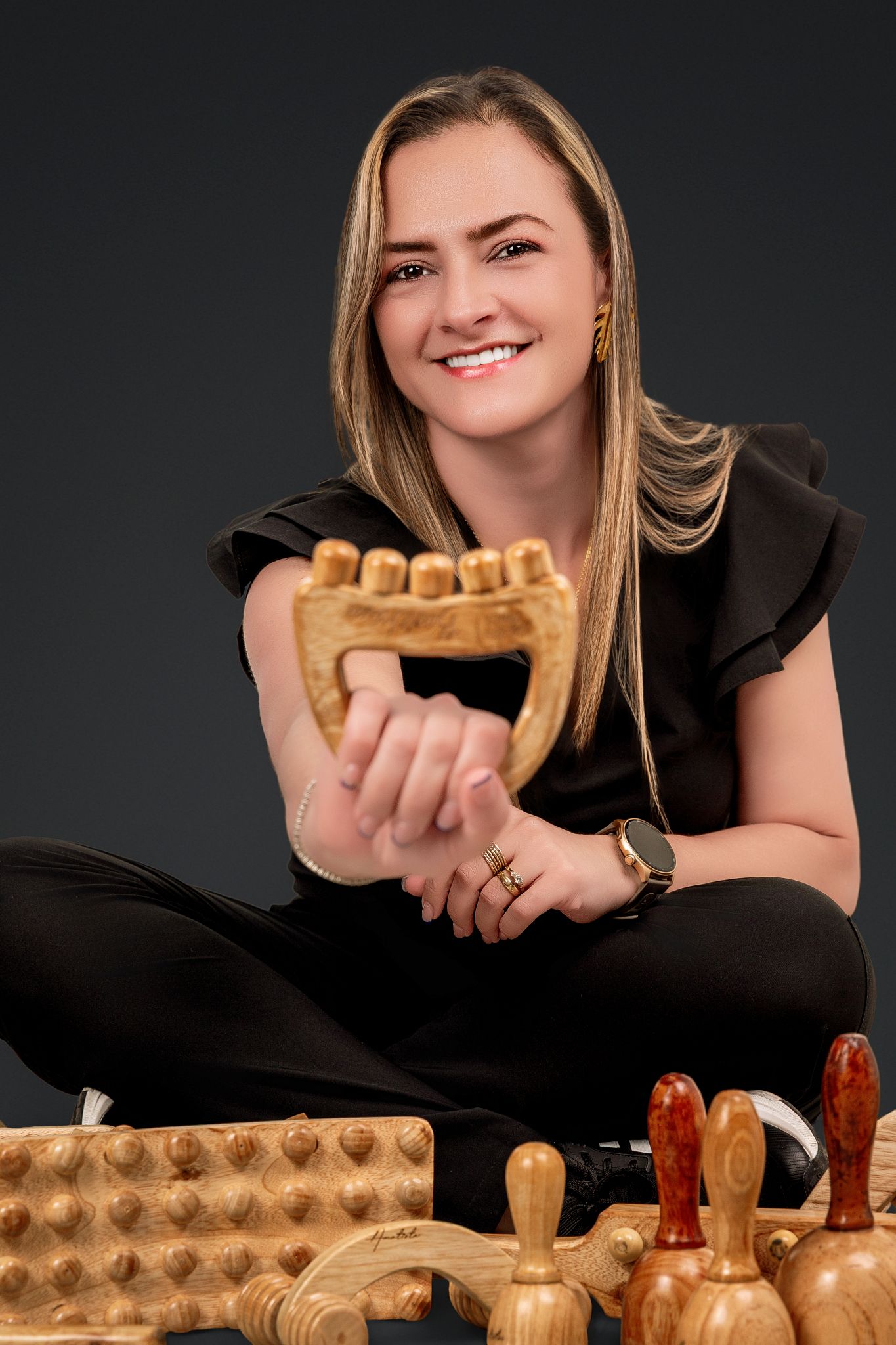 A cheerful person in black clothing holds a wooden waffle mold with vintage kitchen implements displayed below.