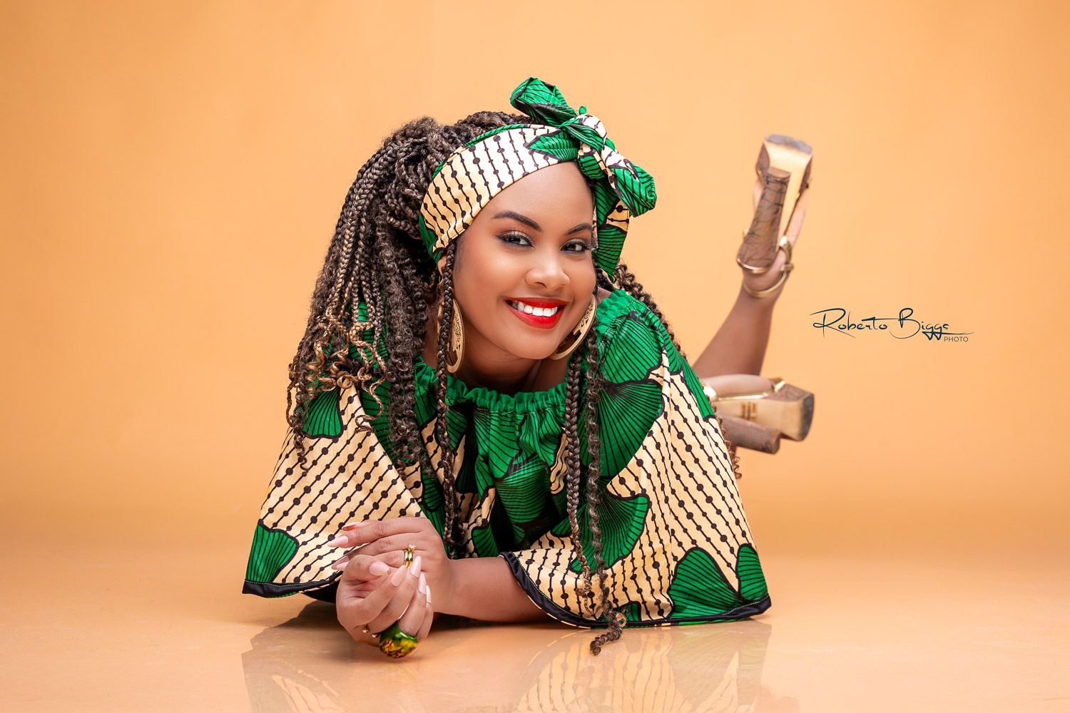 Woman in green African print outfit with gold accessories poses gracefully in a professional studio photo shoot.