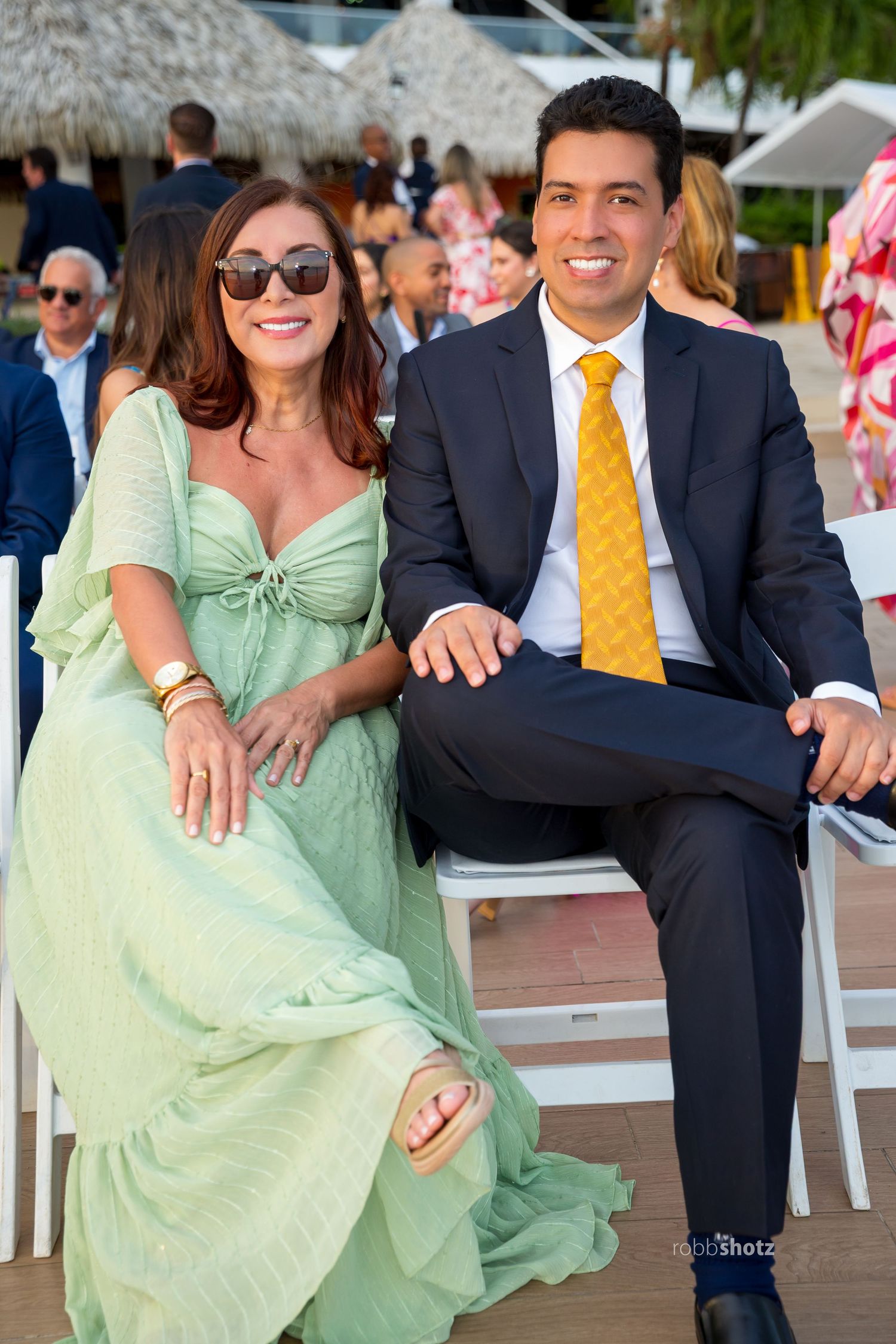 A couple seated at an outdoor event, with a navy suit and mint green dress coordinating their outfits.