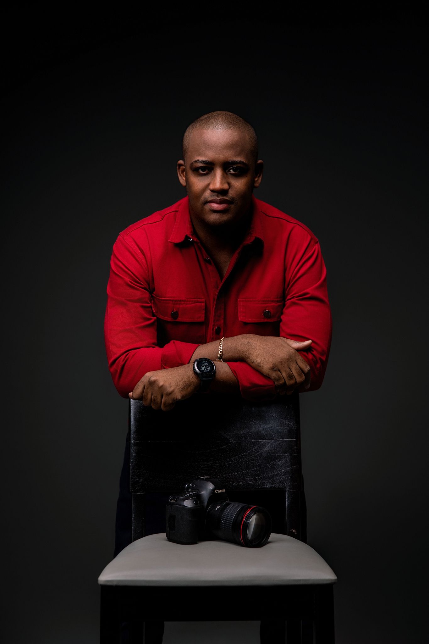 Professional portrait session against dark background featuring someone in a red shirt sitting on a white chair.