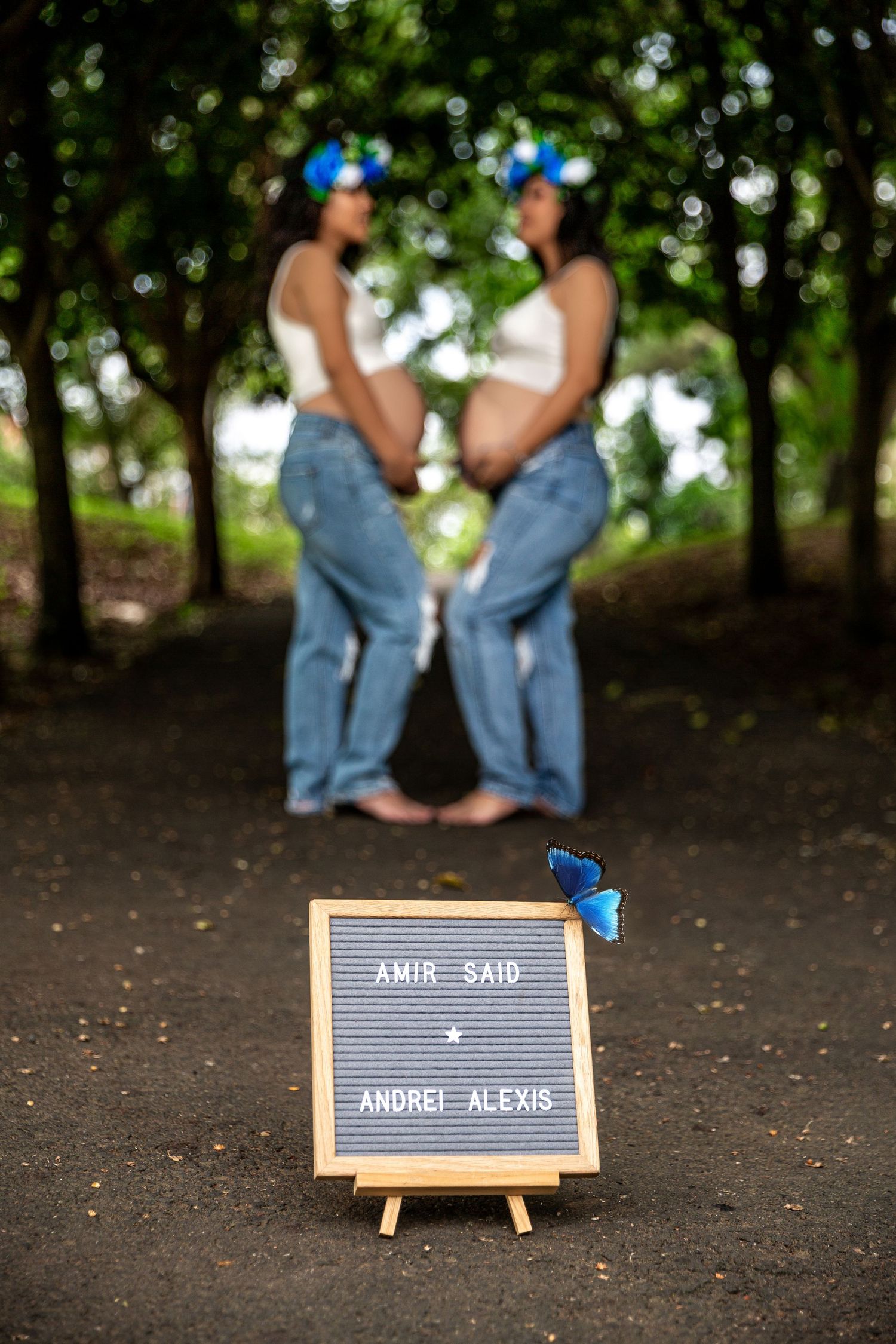 Two people in matching blue outfits stand by a small letterboard sign on an easel decorated with blue butterflies.