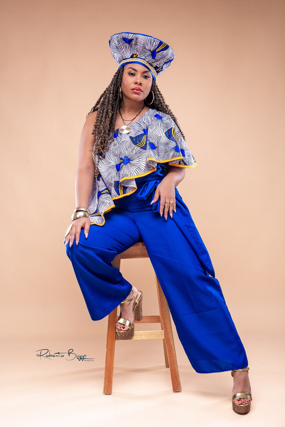 A woman in a blue barrette and matching overalls strikes different poses while sitting on a wooden stool.