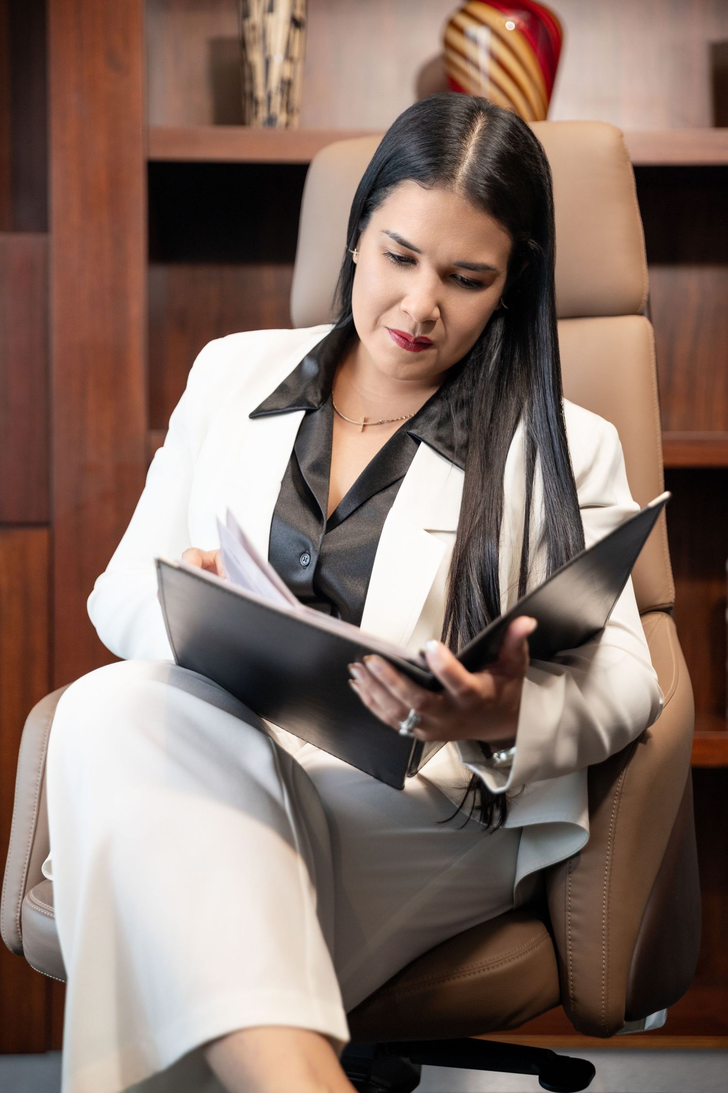 Professional businesswoman in white suit reviewing documents in leather office chair.