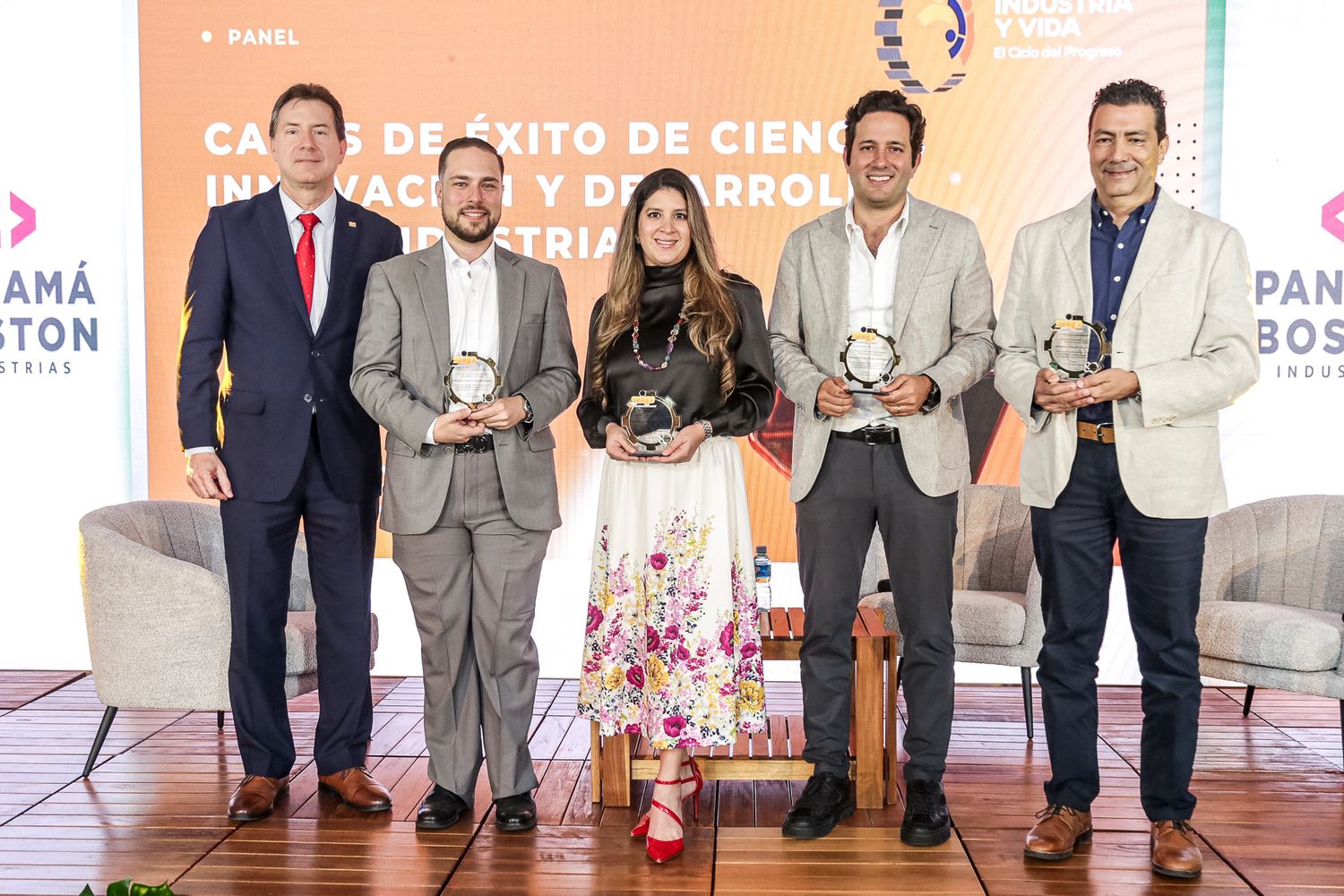 Five business professionals stand together holding awards at a corporate recognition ceremony against a peach-colored backdrop.