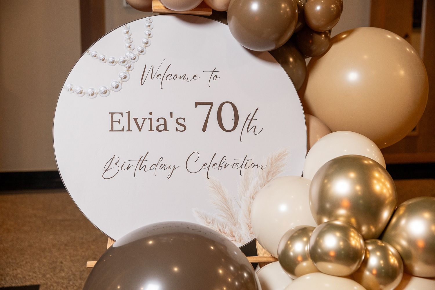 Elegant 70th birthday celebration sign for Elvia surrounded by gold, white, and taupe balloon garland decorations.