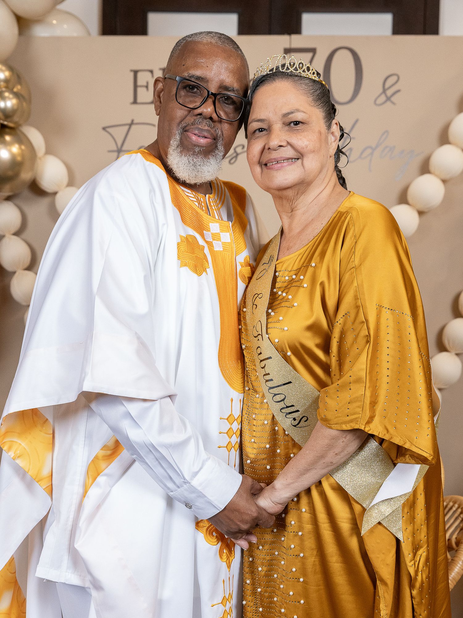Elderly couple in matching gold and white traditional African attire celebrating a 70th birthday party milestone.