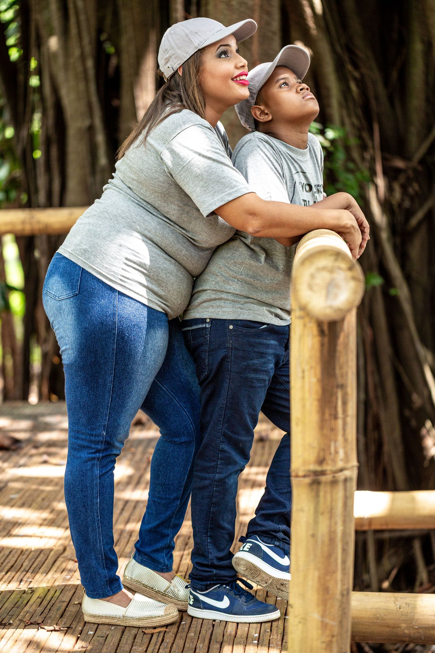 Parent and child in matching gray outfits look up while standing on wooden deck.