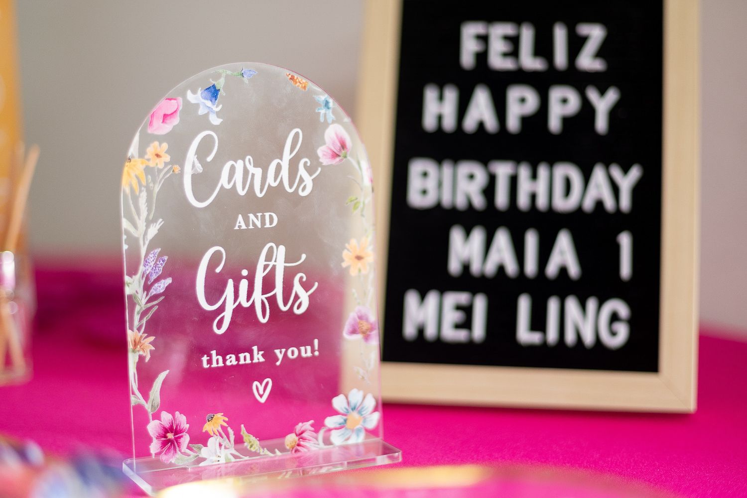 Acrylic Cards and Gifts sign with floral details beside a letter board reading Feliz Happy Birthday Maia and Mei Ling.
