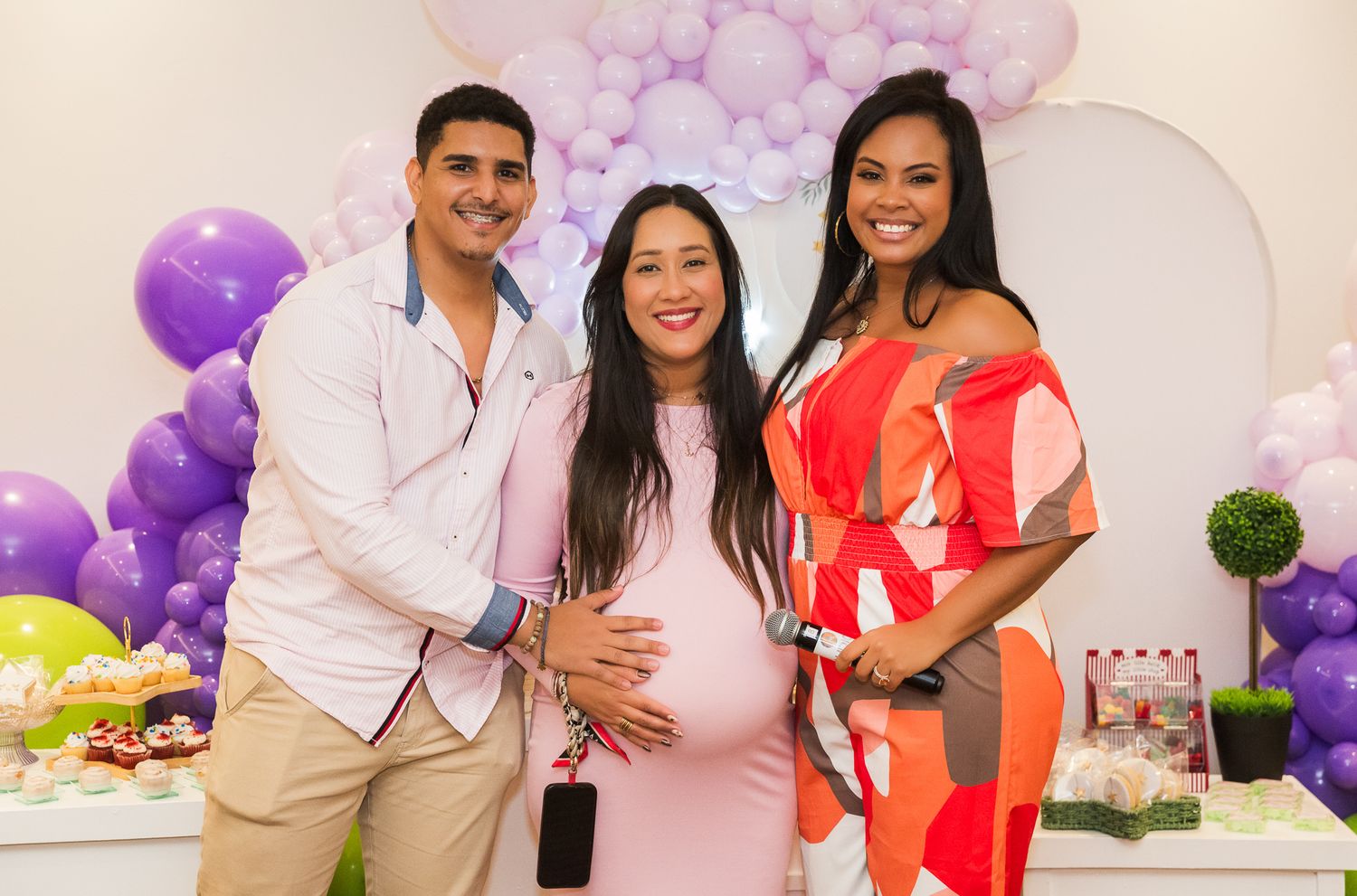People celebrate at a baby shower with purple balloon decorations and festive party decor in the background.
