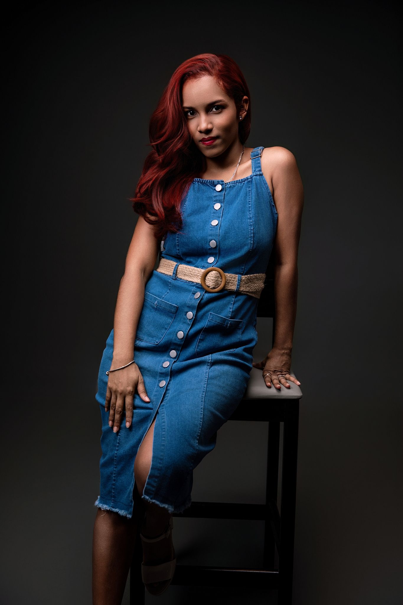 Model in denim button-up dress and brown belt poses against dark background in fashion photoshoot series.