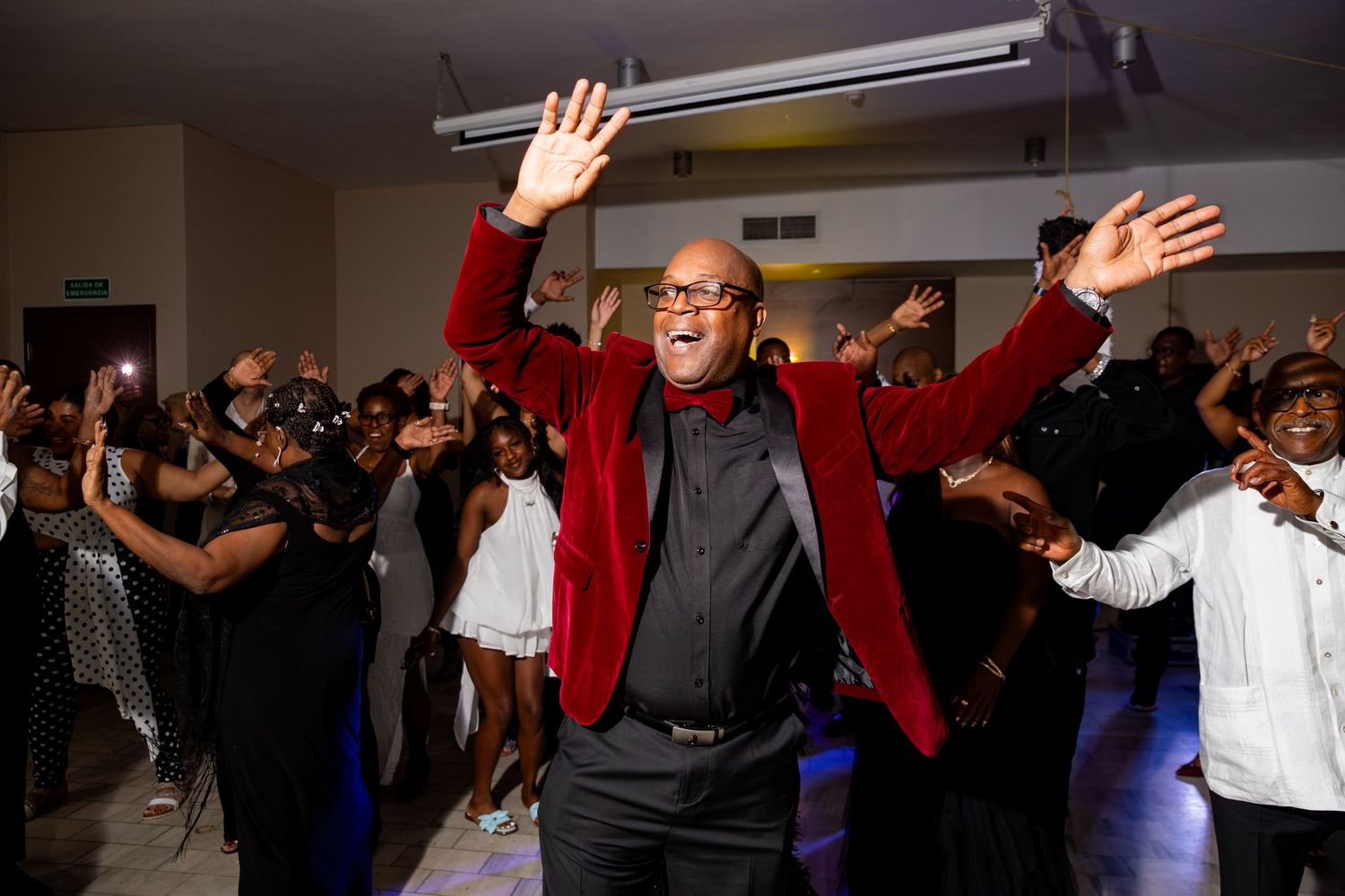 Man in red velvet blazer dancing joyfully with hands raised at a lively party celebration.