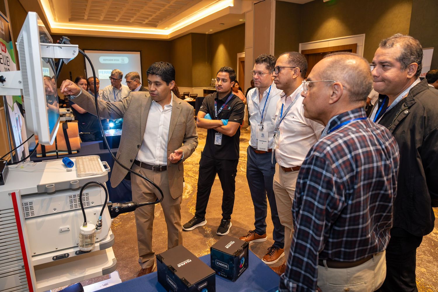Professionals gathered around a technology display at a conference, examining equipment and engaging in discussion.