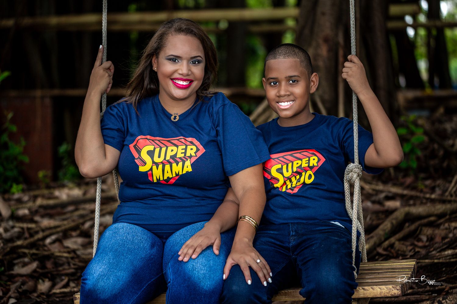 Two people in matching blue superhero themed t-shirts sitting on rustic wooden steps outdoors.