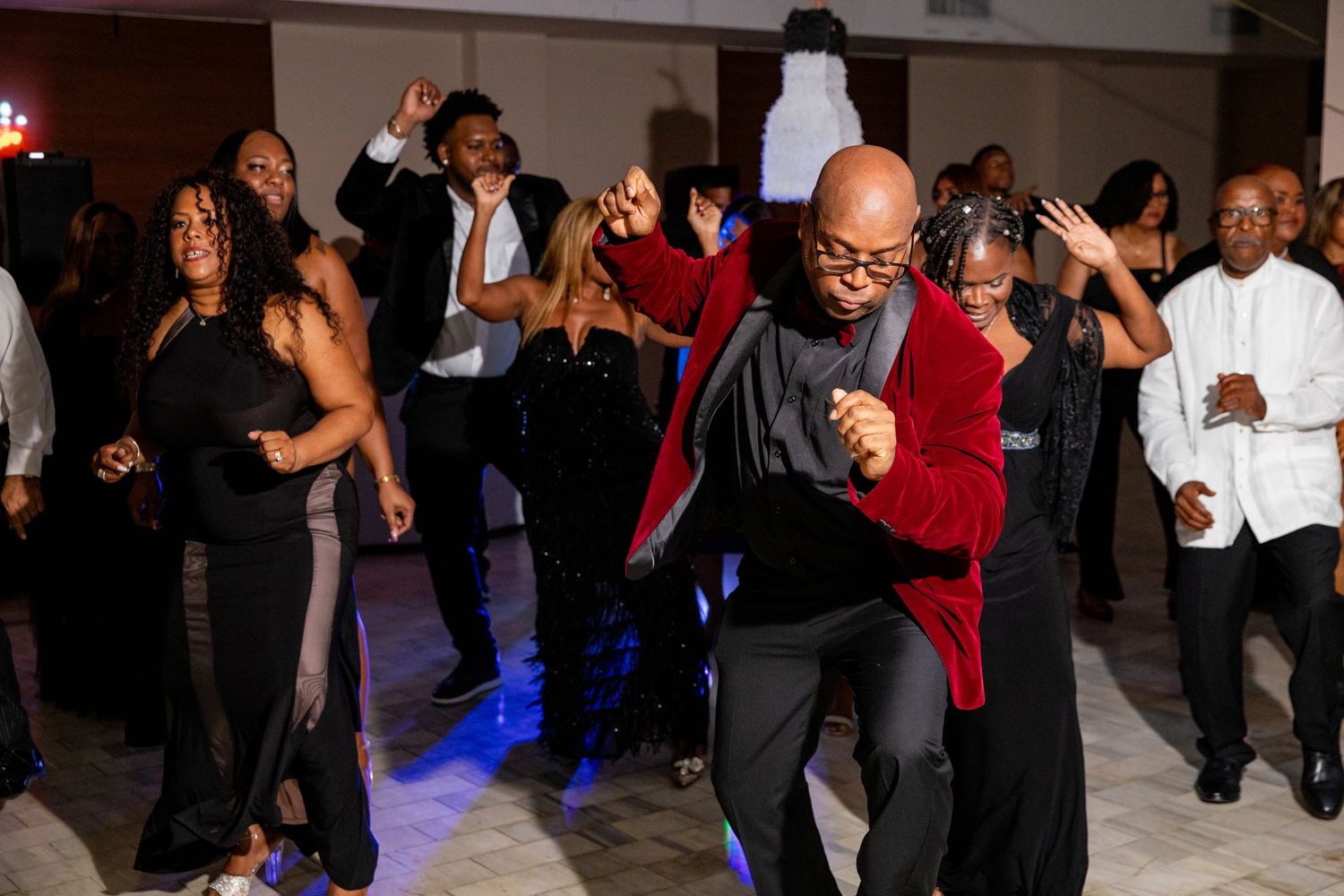 Guests dancing energetically at a formal event, wearing elegant black and red attire on a decorated dance floor.