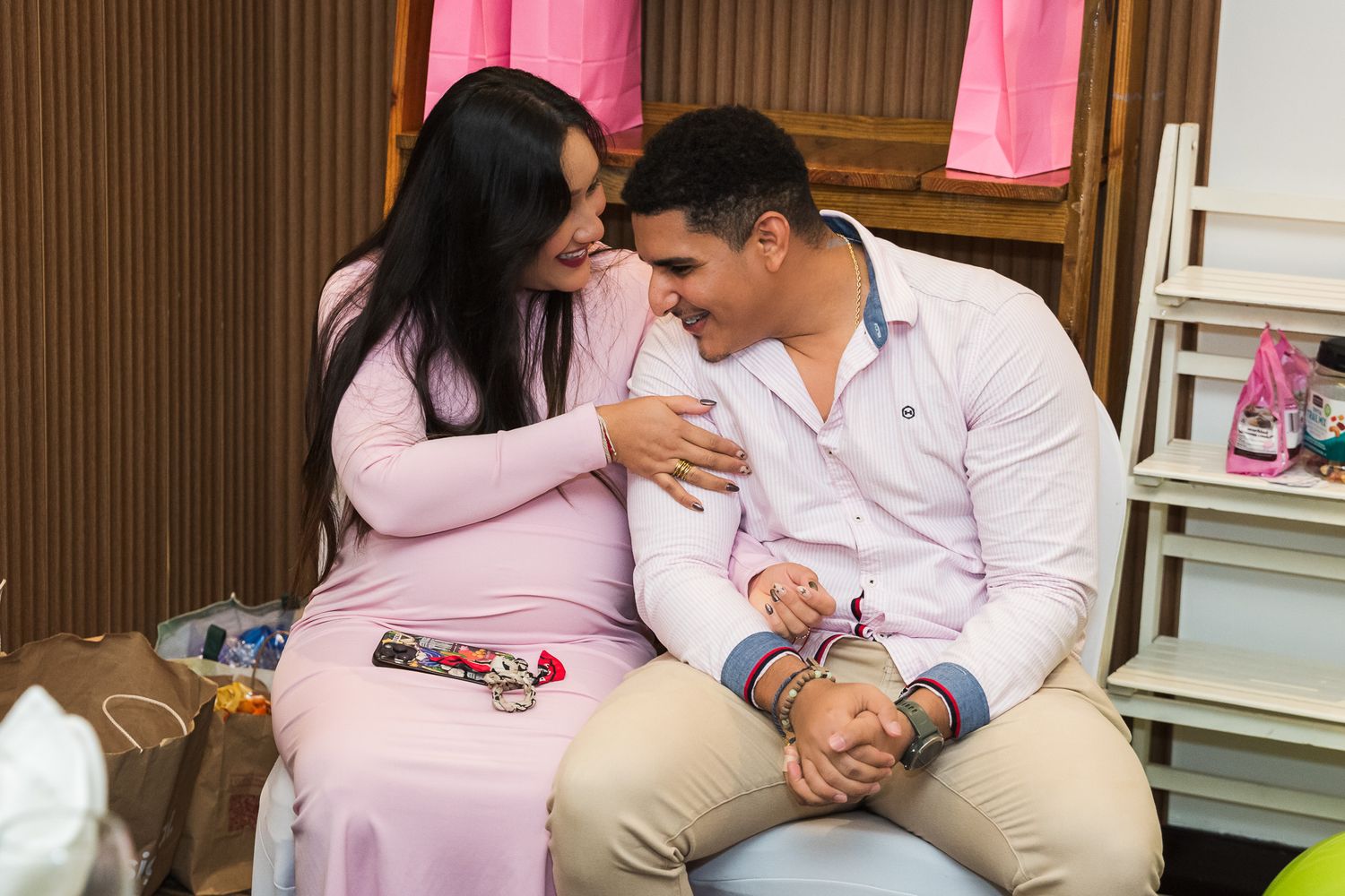 Two people share an intimate moment while sitting together in a room with pink decor and wooden walls.