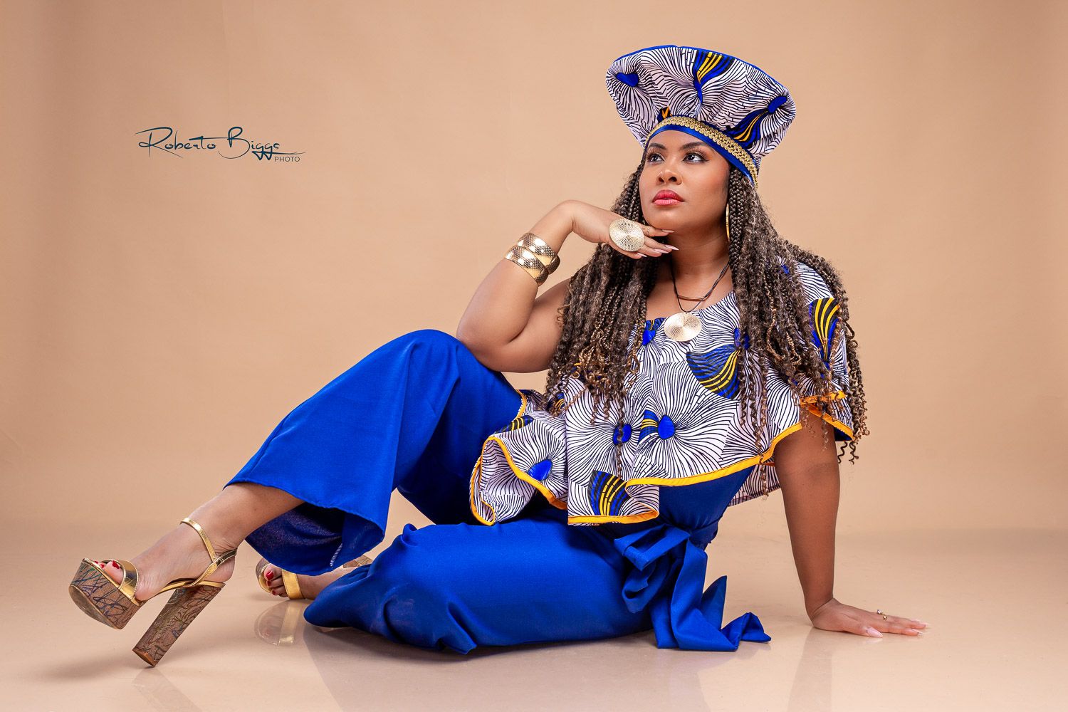 A model poses in a bright blue outfit with matching print accessories and high heels against a beige background.